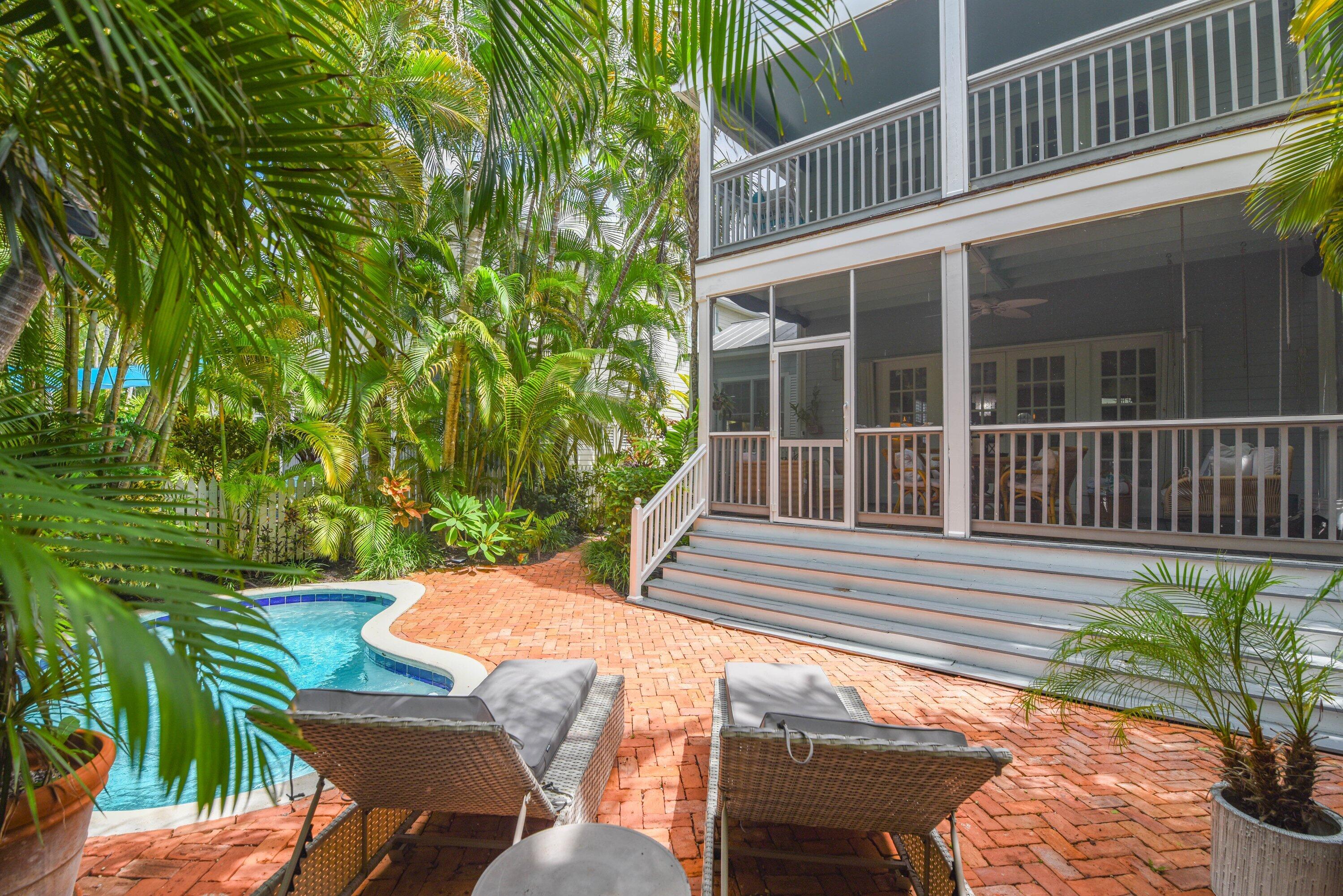 Tropical backyard with a curved pool, brick patio, and screened porch.