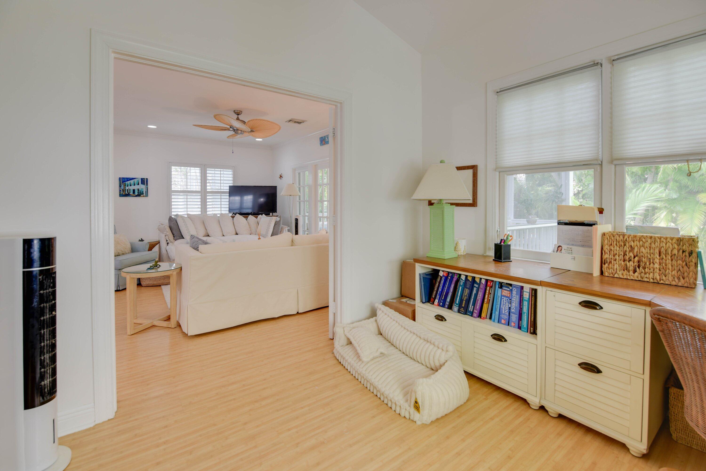 Bright sitting area with built-in book cabinet and windows, opening onto a living room with cream sofas.