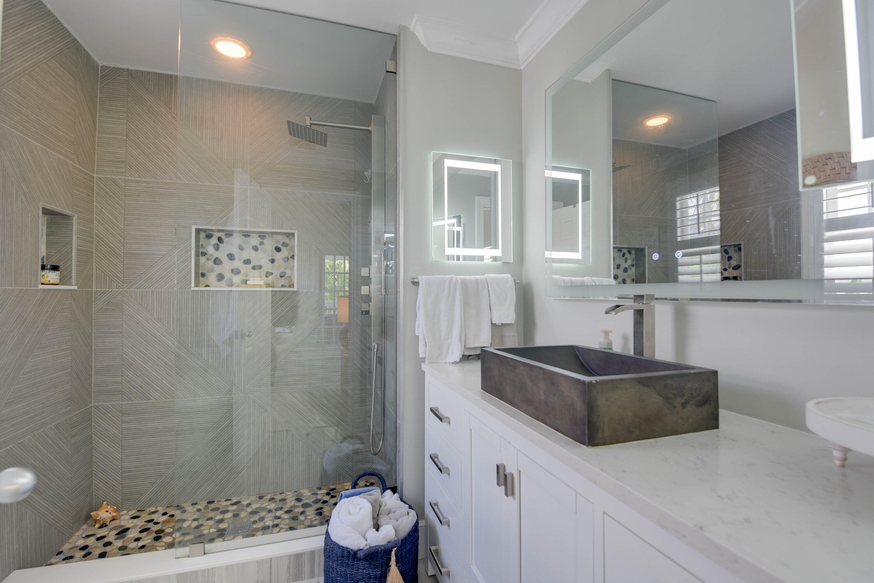 Modern bathroom with a pebble-accented glass shower and dark vessel sink.