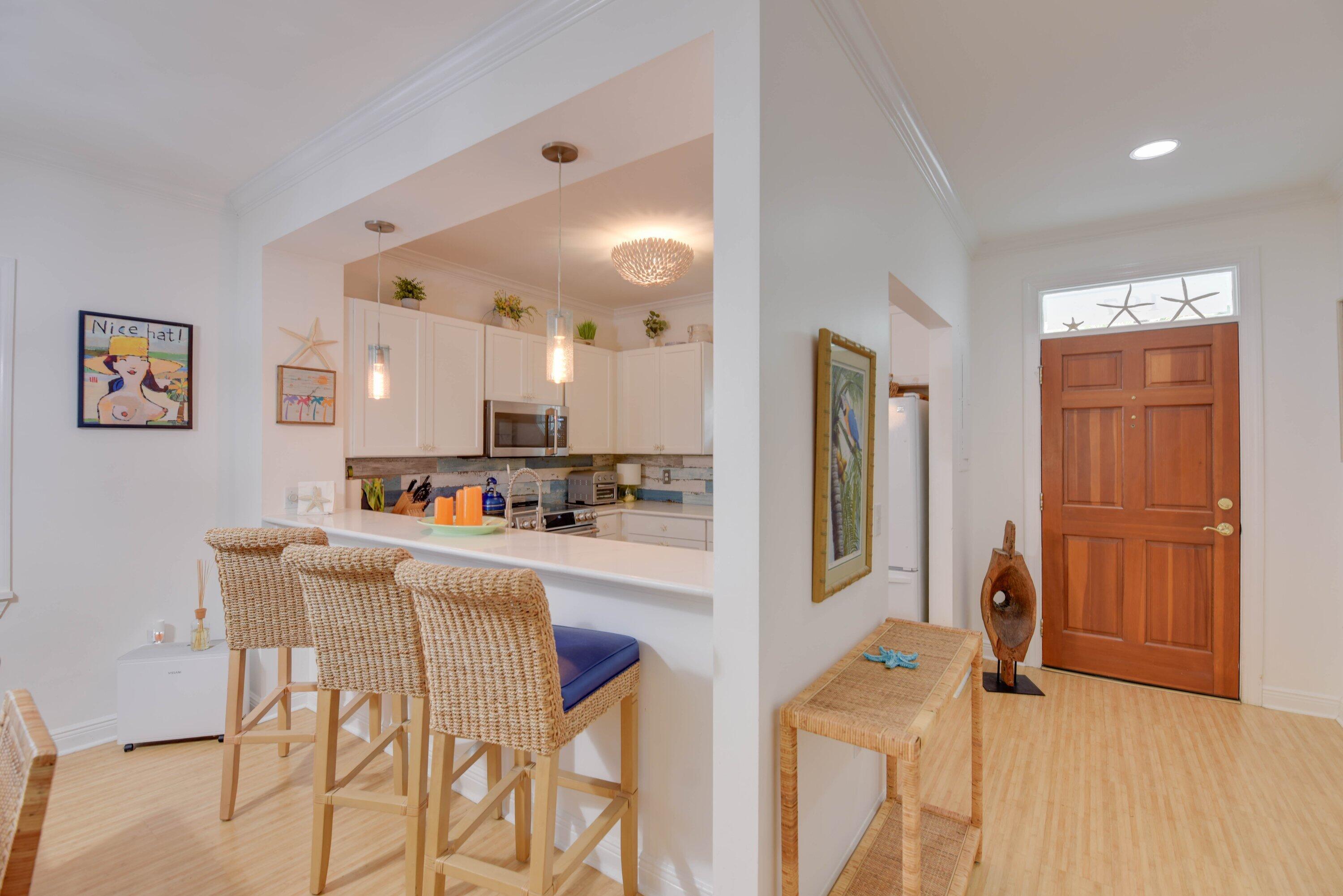 Open kitchen and entryway with woven breakfast bar stools and a paneled wood front door.