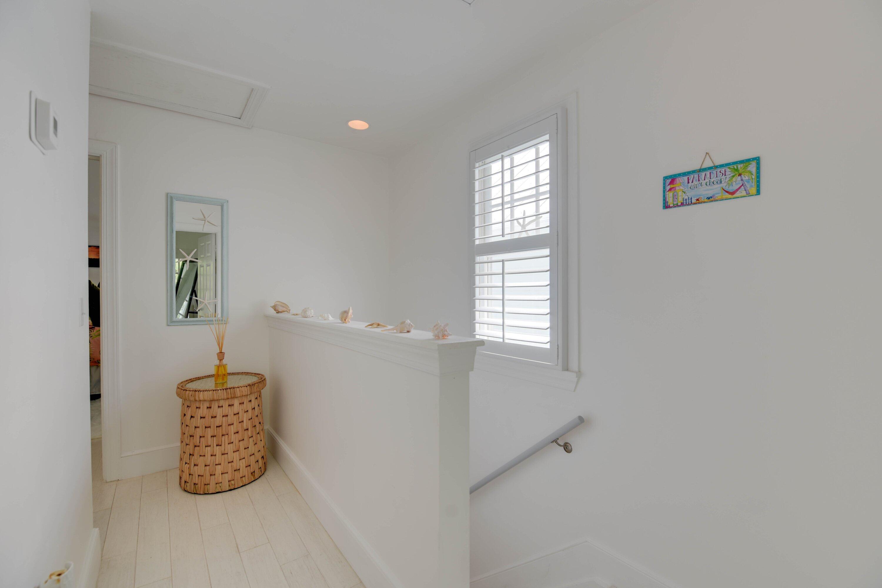 Bright landing with a shuttered window, seashell display, and woven rattan table.