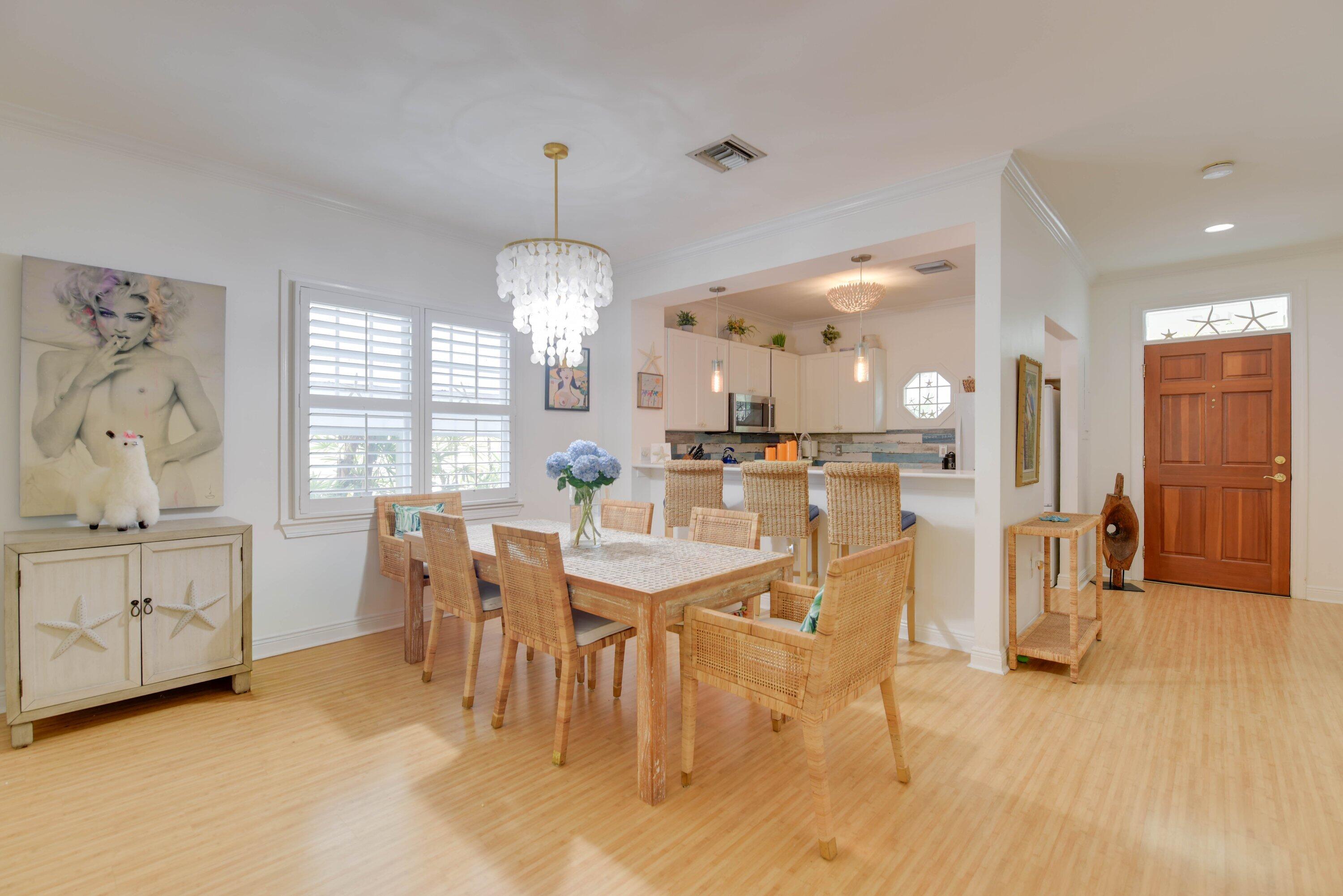 Dining room with woven-wood furniture, plantation shutters, and an open kitchen.