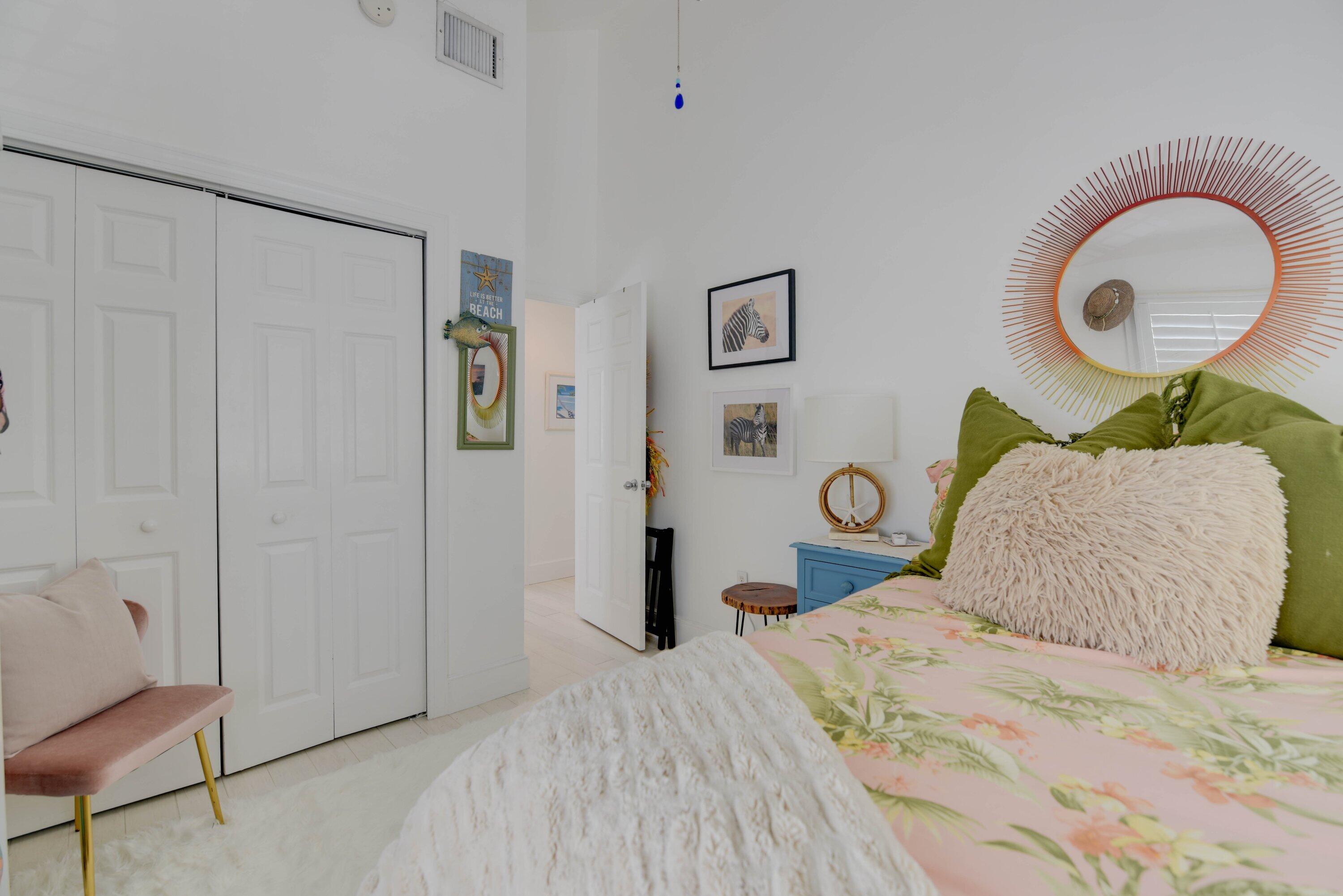 Bedroom with tropical floral bedding, green pillows, and a large sunburst mirror.