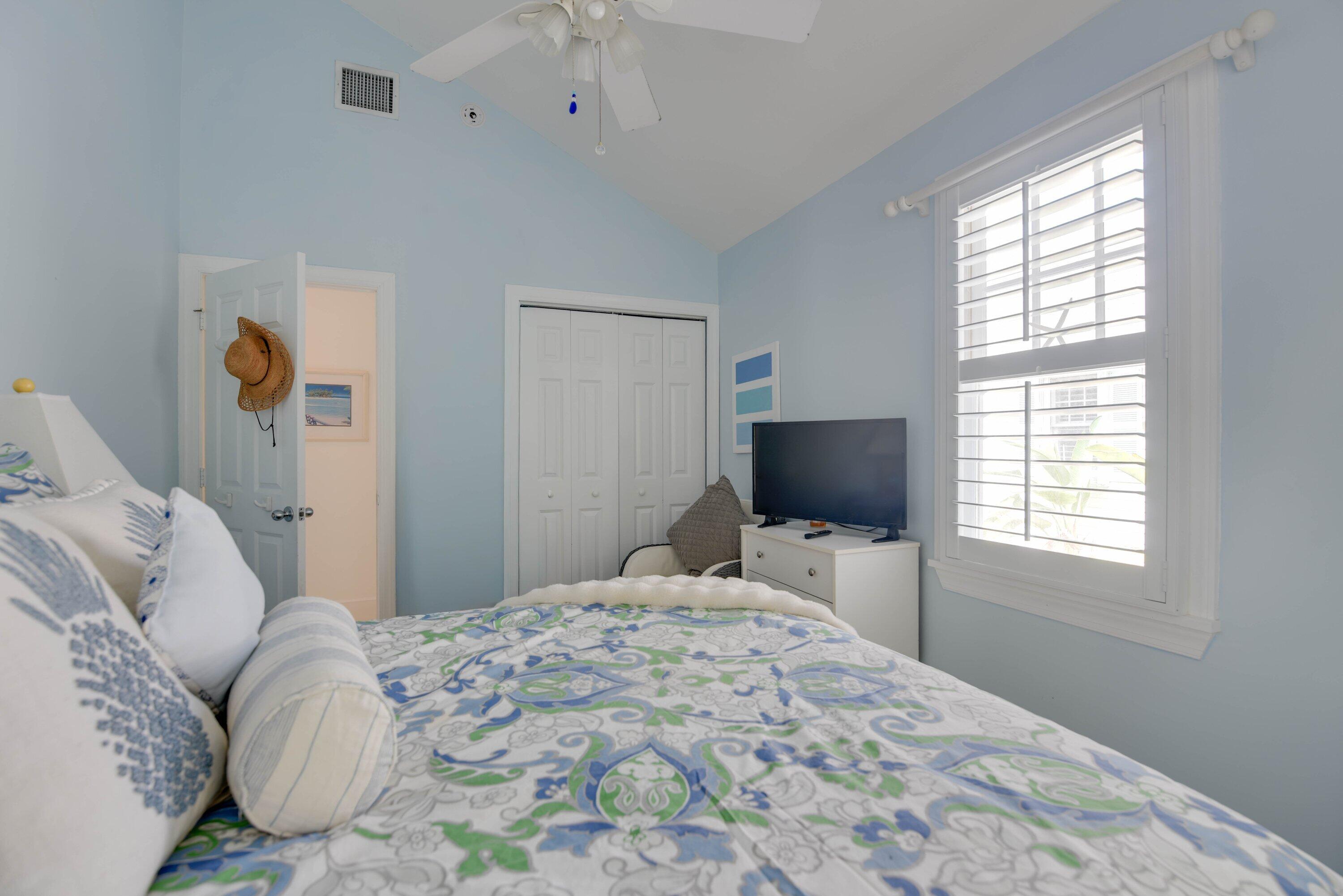 Bedroom with blue walls, patterned bedding, and a large shuttered window.
