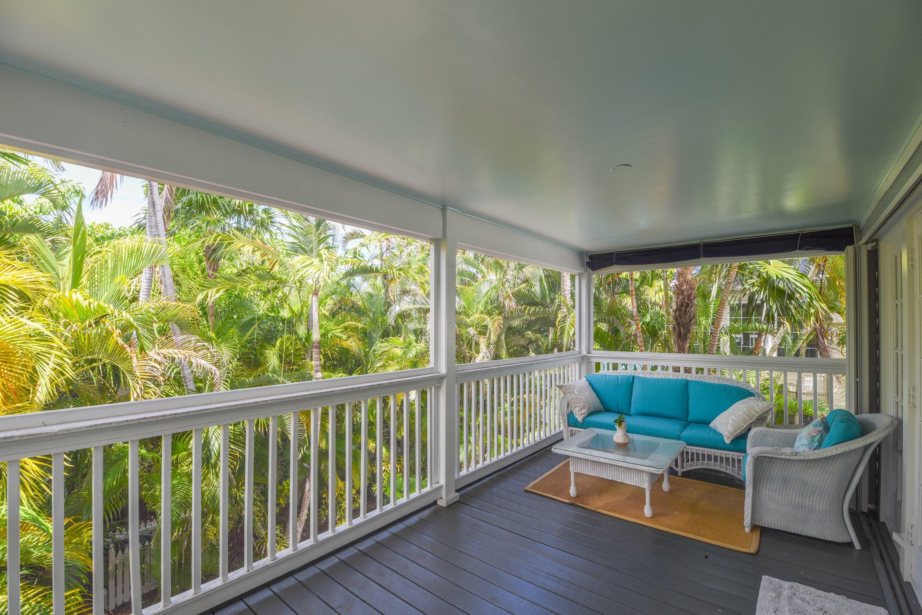 Covered porch with turquoise wicker seating, gray decking, and surrounding palms.
