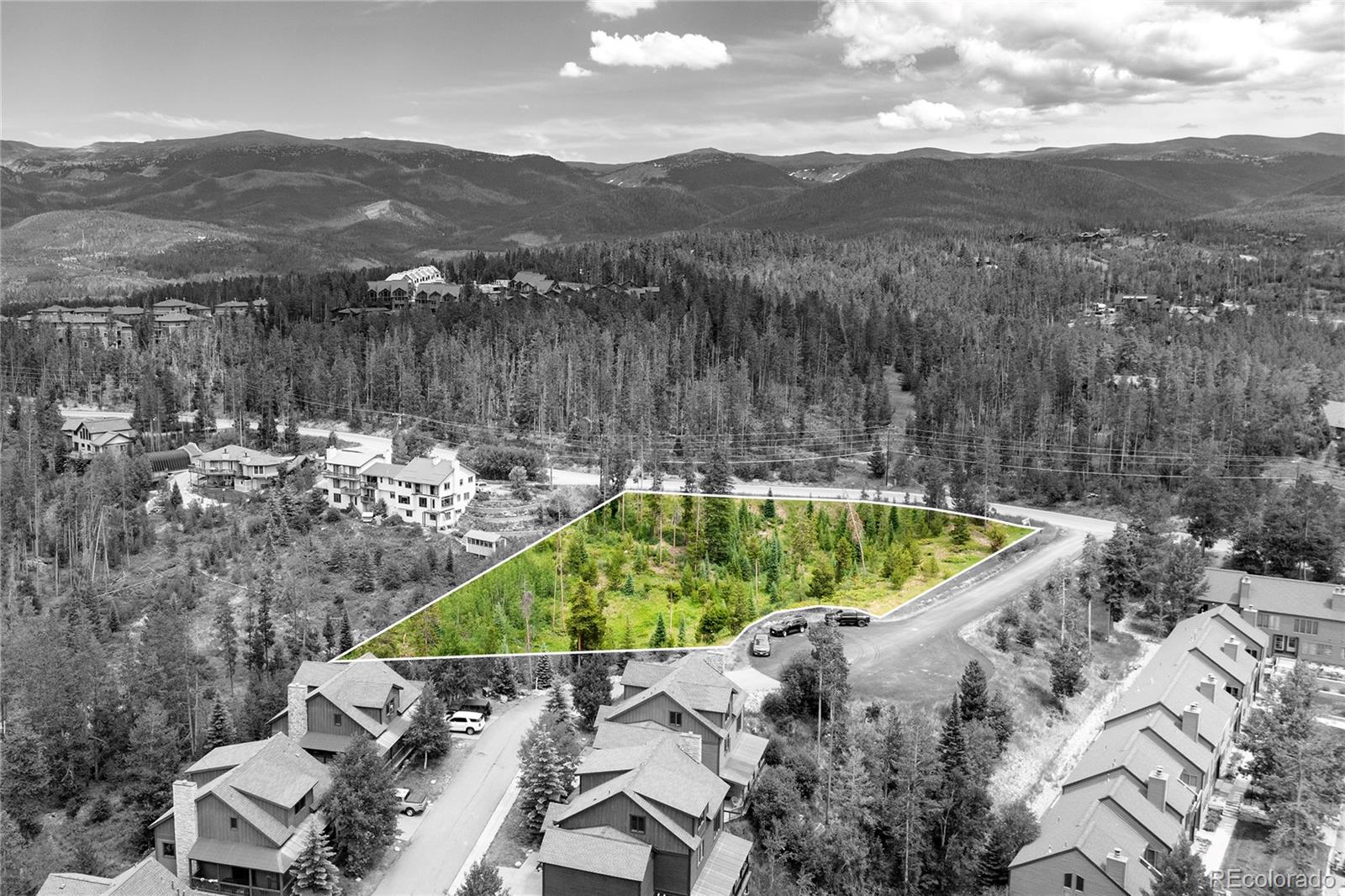 Aerial view of a wooded vacant lot outlined in green, with mountain ranges in the distance.