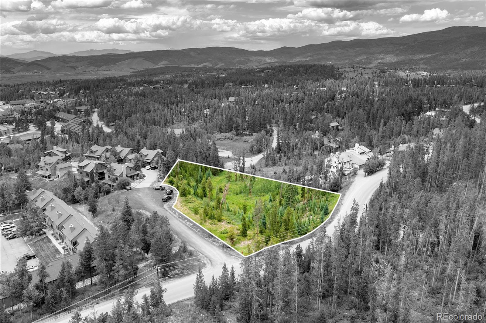 Aerial view of a wooded vacant lot outlined in white, surrounded by homes, forest, and mountains.