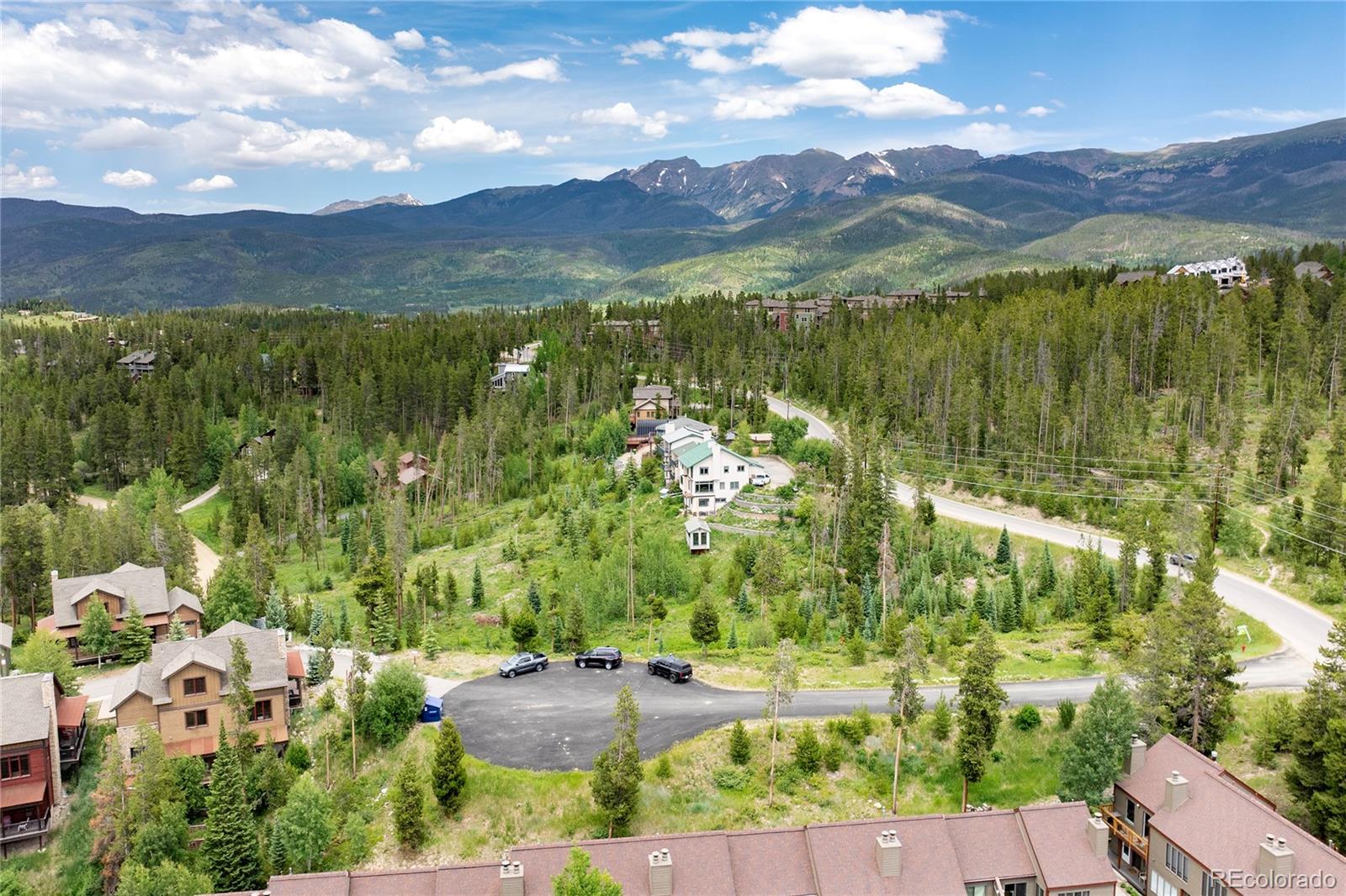 Aerial view of a home among forested hills, with winding roads and mountains beyond.
