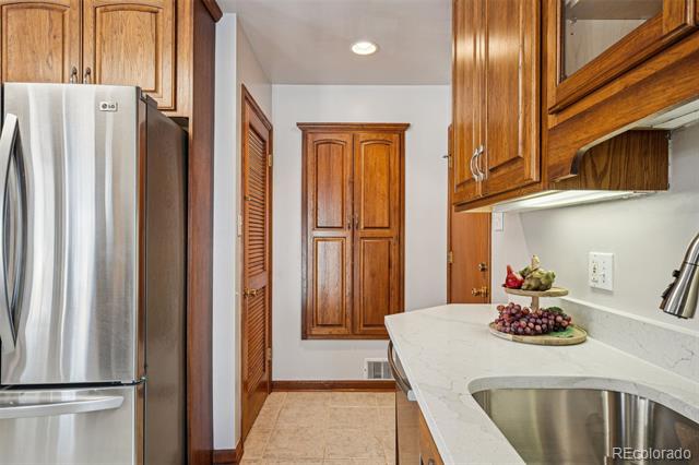 Kitchen with warm wood cabinetry, stainless-steel refrigerator, and curved white countertop with an undermount sink.