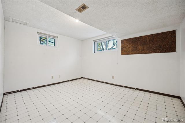Empty room with white tiled floor, two high windows, and a brown wall panel.