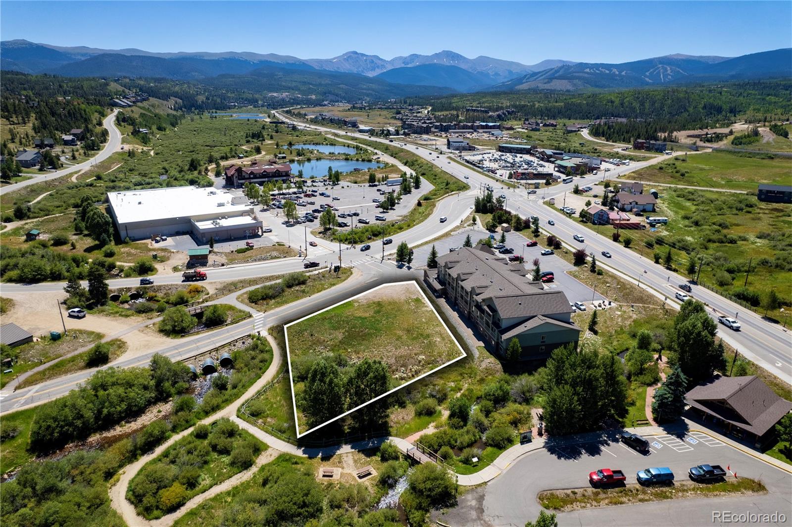 Aerial view of an outlined vacant lot beside a creek, with roads and mountains beyond.