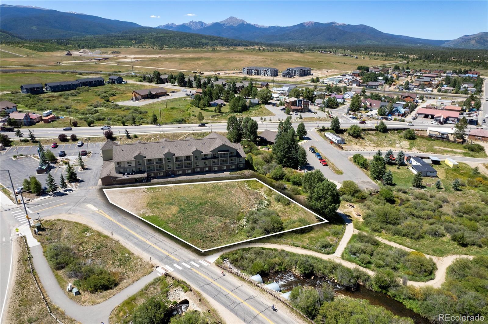Aerial view of a vacant lot outlined beside a road, with Fraser buildings and mountains beyond.