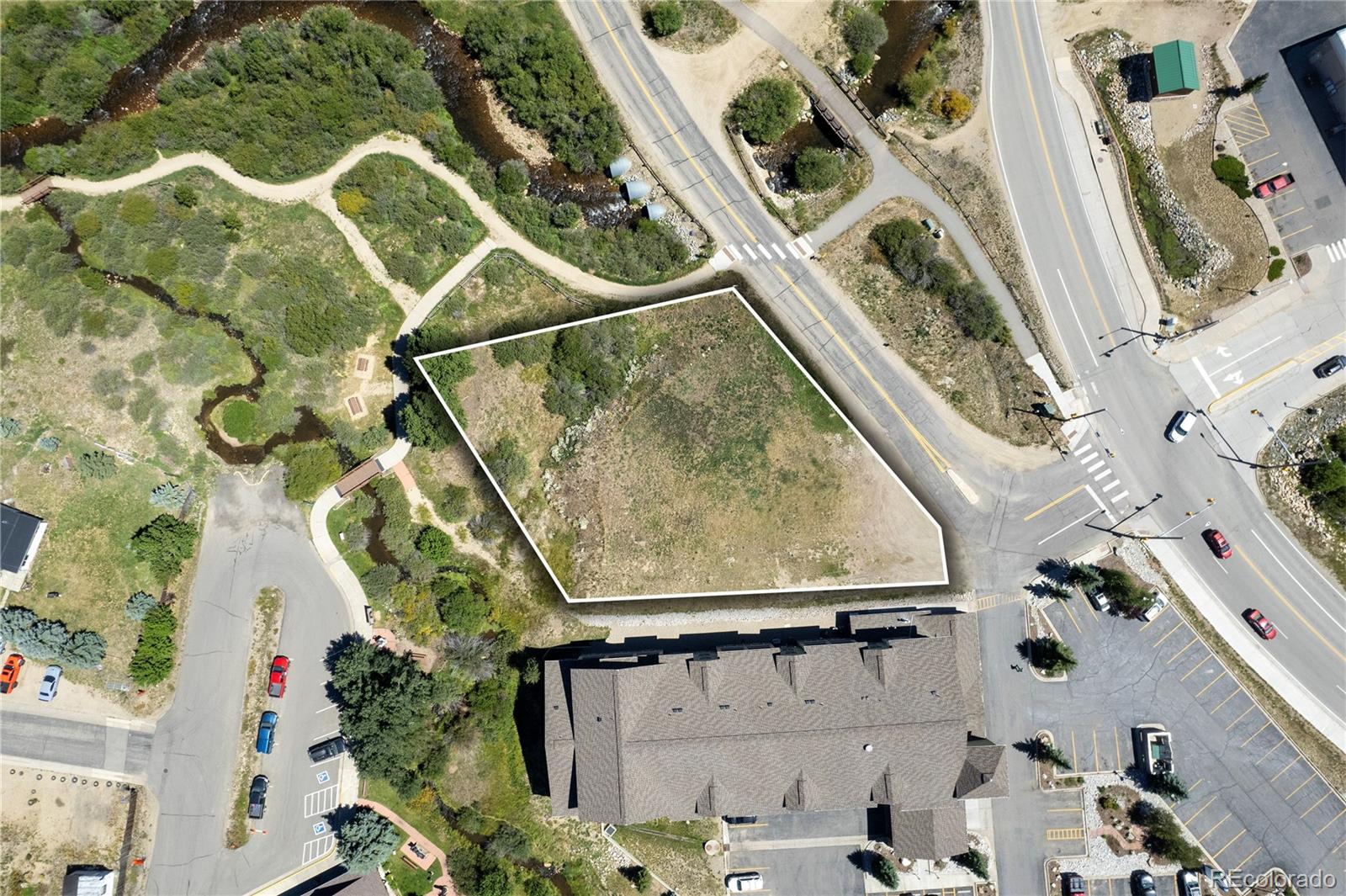 Aerial view of a vacant parcel outlined beside a creek, walking path, and road intersection.