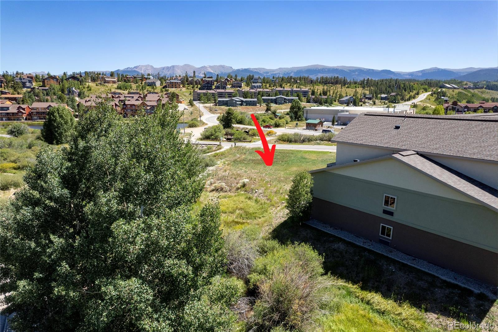Vacant grassy lot marked with a red arrow, with homes and mountains in the distance.