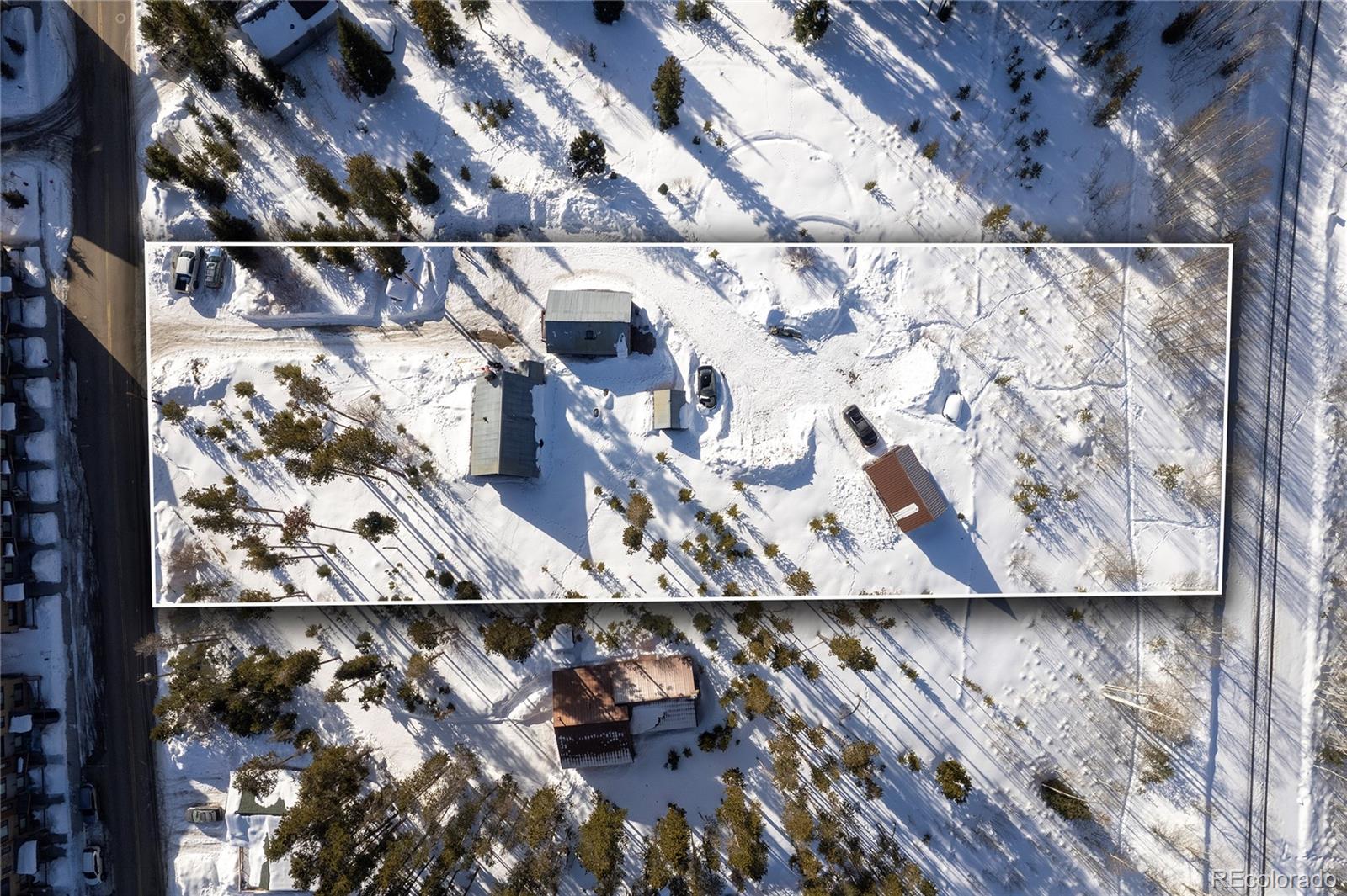 Aerial view of a snow-covered, tree-lined property outlined in white, with several buildings.