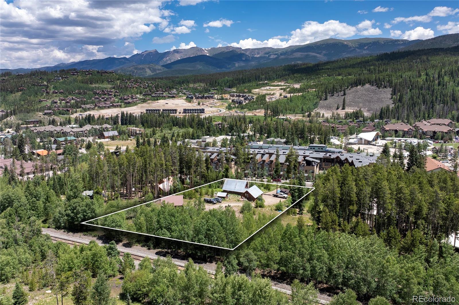 Aerial view of a wooded property parcel outlined against mountain scenery and nearby homes.