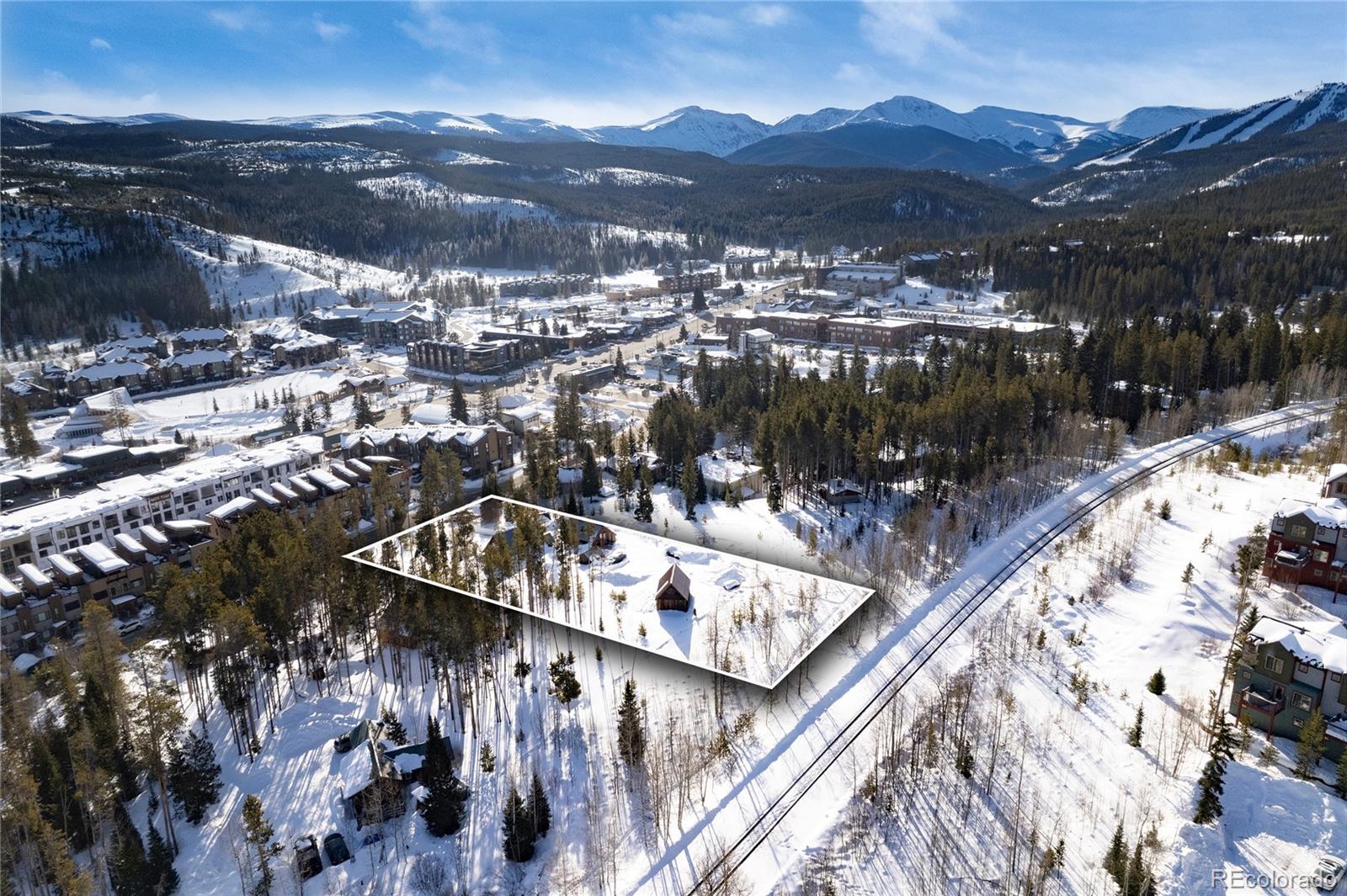 Snow-covered wooded parcel outlined in white, with a small cabin and mountain town beyond.