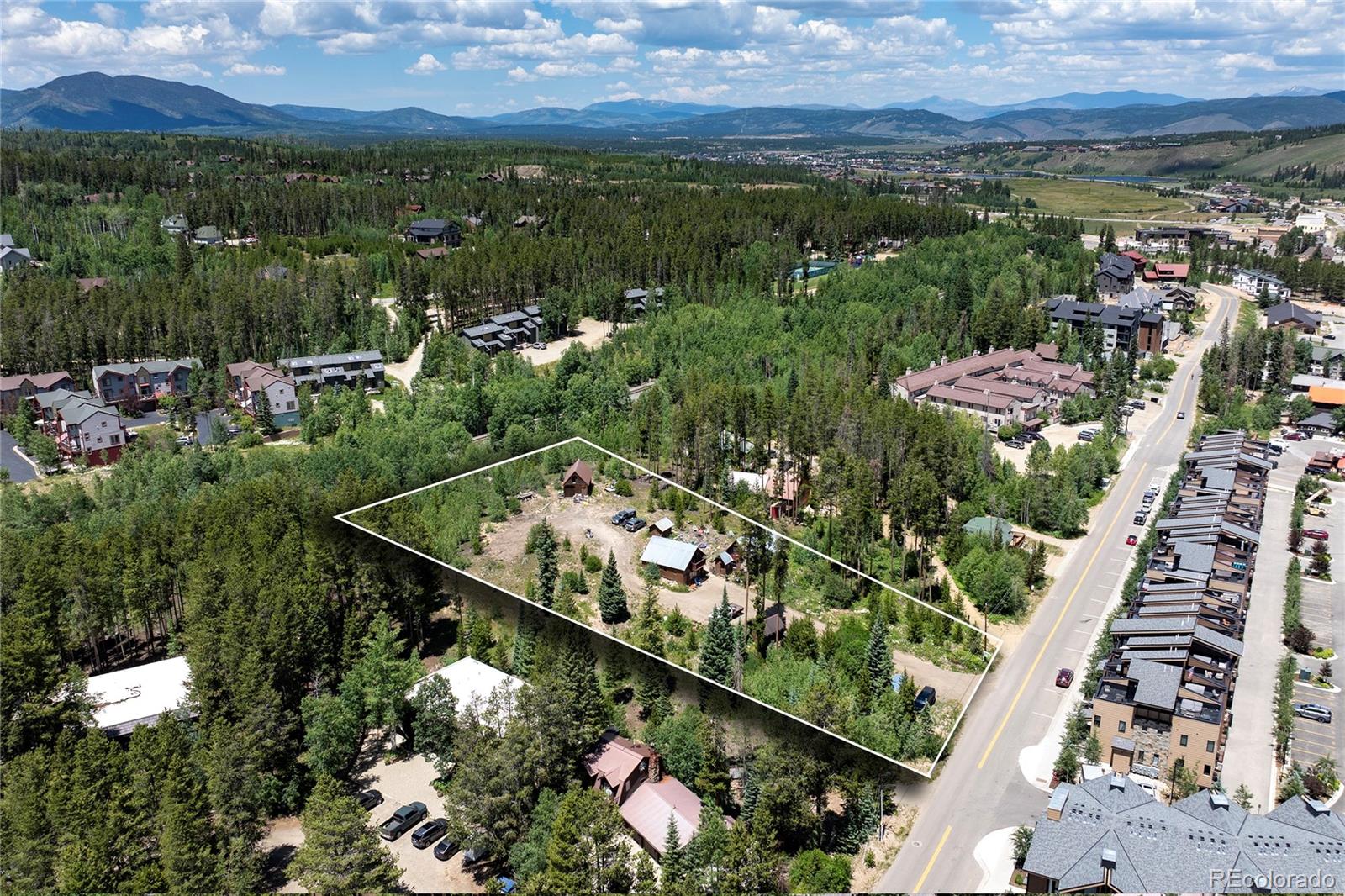 Aerial view of a wooded property outlined beside a road, with mountain ranges in the distance.