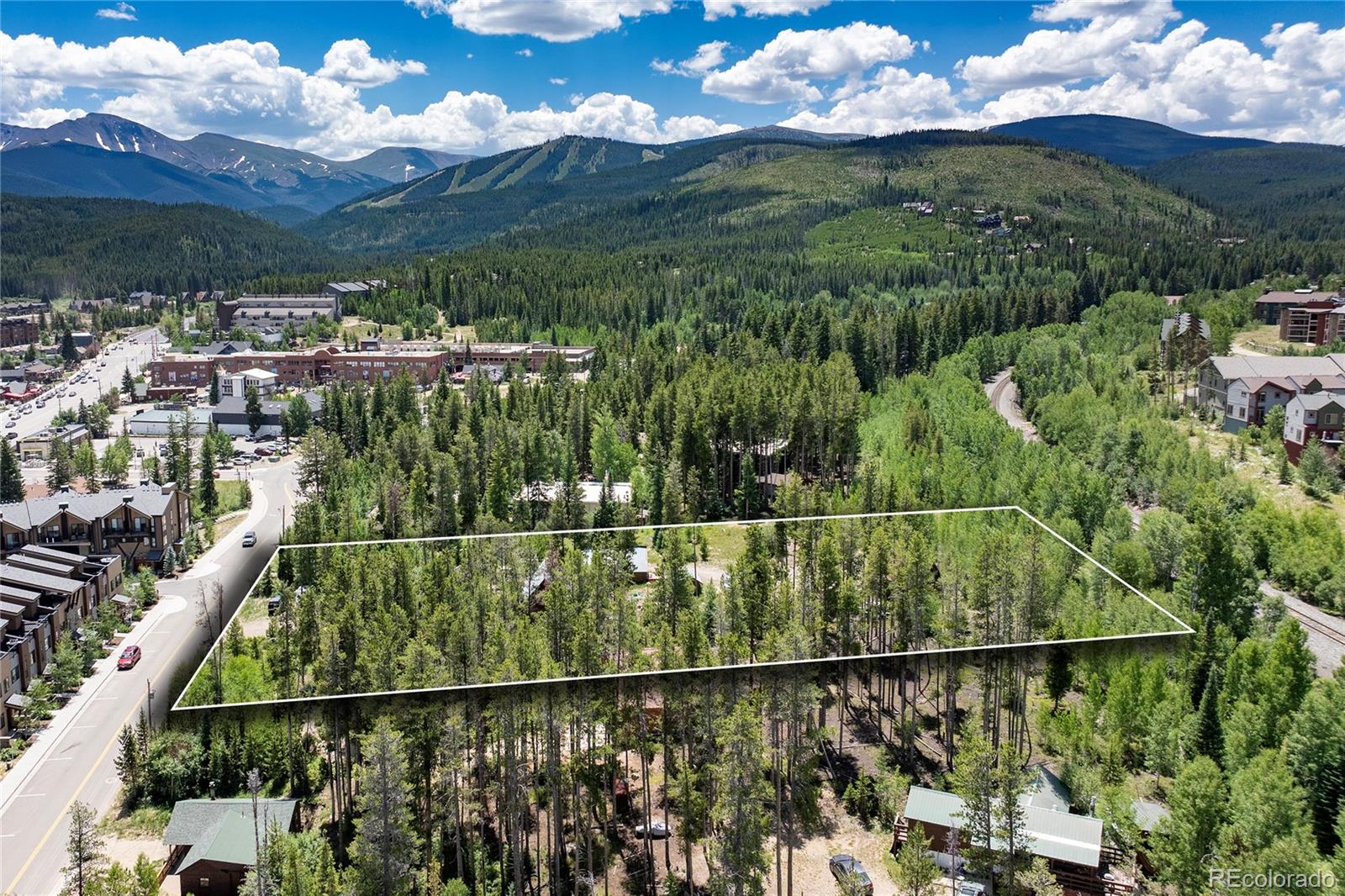 Aerial view of a wooded lot outlined against a mountain town and distant peaks.