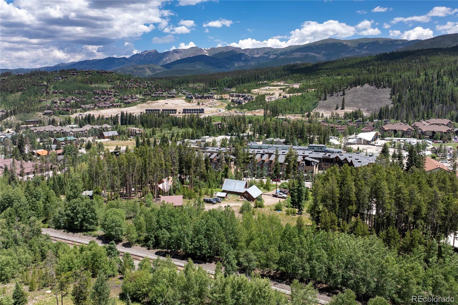 Aerial view of a mountain resort community, with forest, railway tracks, and mountain ranges beyond.