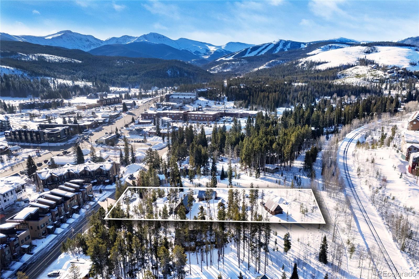 Snowy wooded parcel outlined in white, with Winter Park homes and mountain peaks beyond.