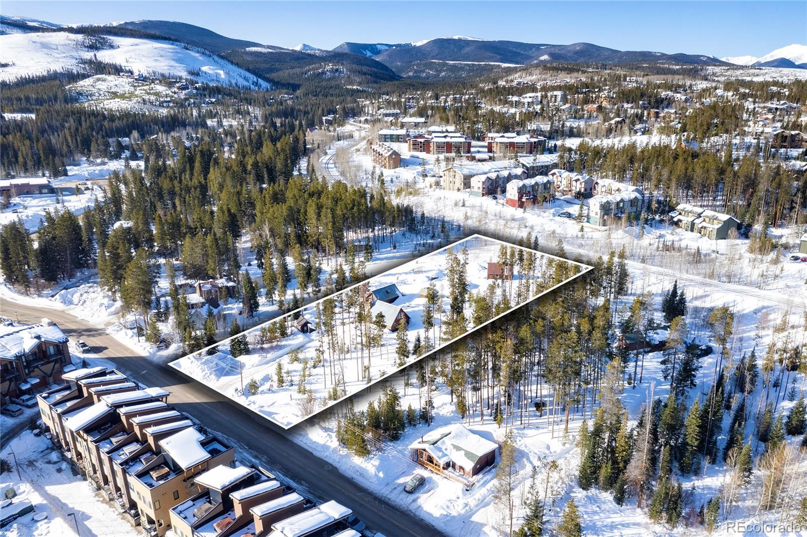 Aerial view of a snow-covered Winter Park property outlined among pine trees, homes, and mountain scenery.