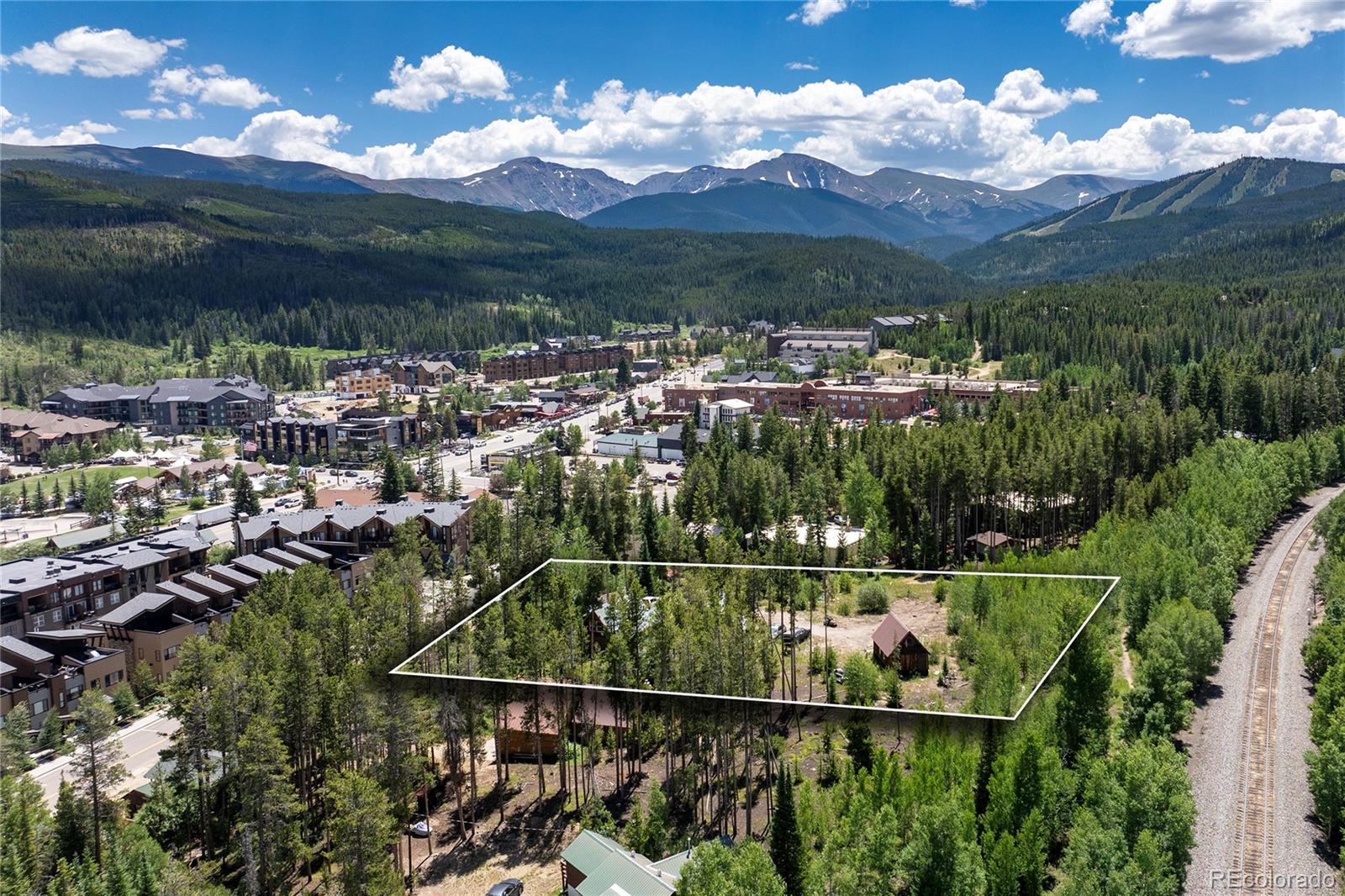 Aerial view of a wooded, outlined parcel with Winter Park buildings and mountains beyond.