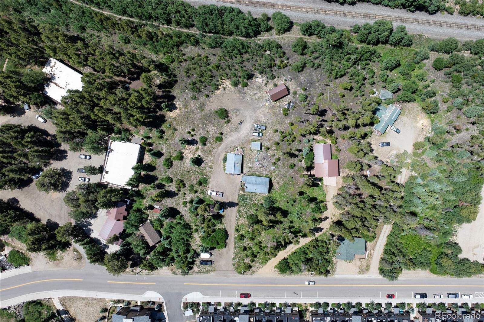 Aerial view of a wooded property with scattered buildings, a central clearing, and railroad tracks along the north edge.