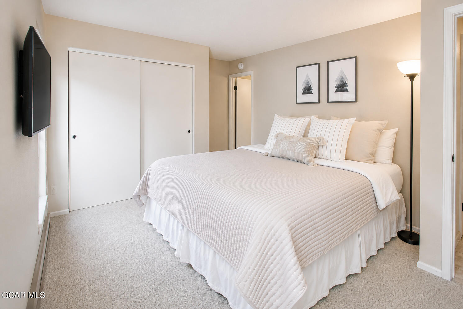 Bright bedroom with a neatly made white bed, sliding closet doors, and framed tree prints.