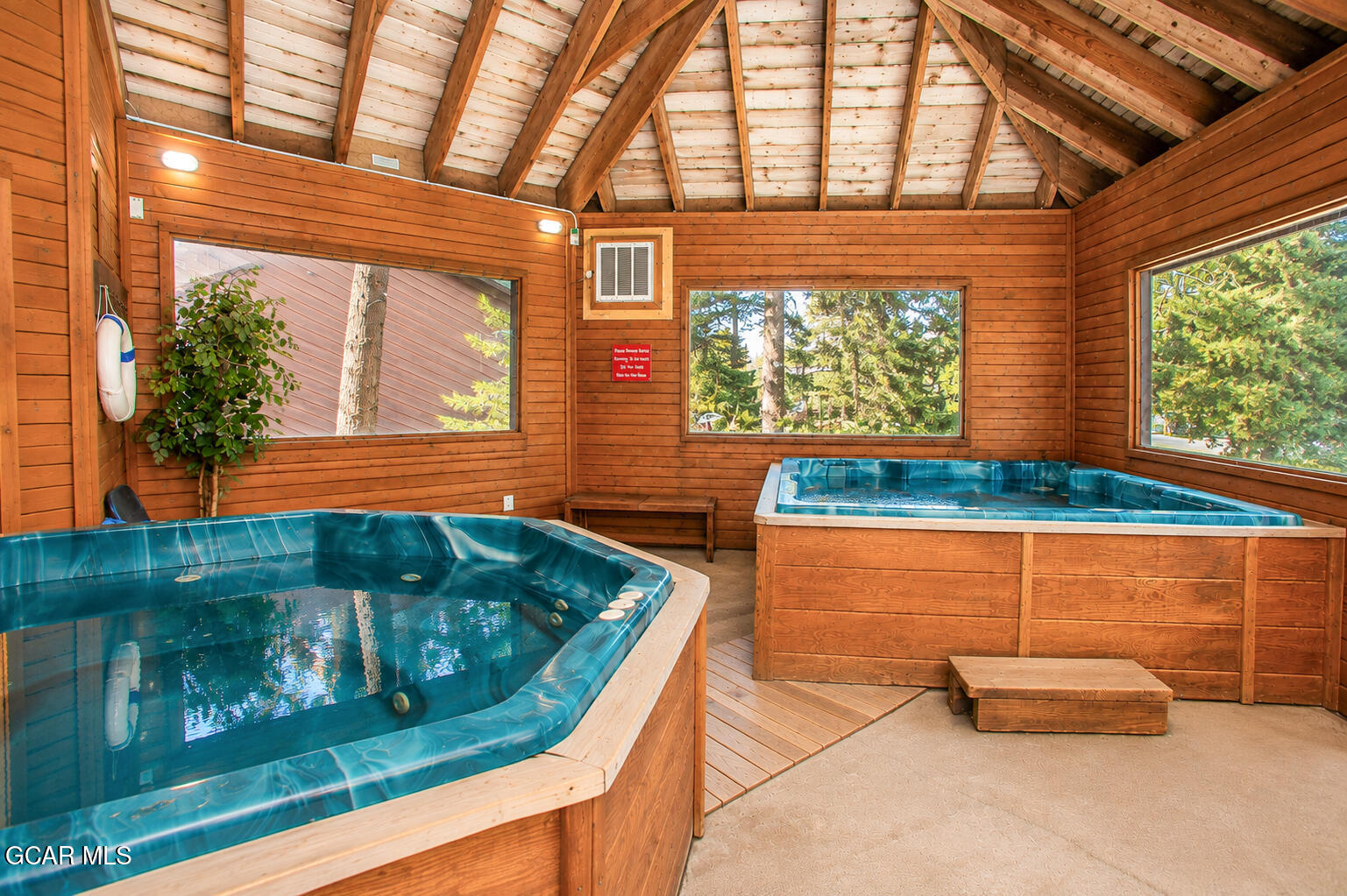 Indoor hot tub room with two blue spas and a vaulted wood-paneled ceiling.