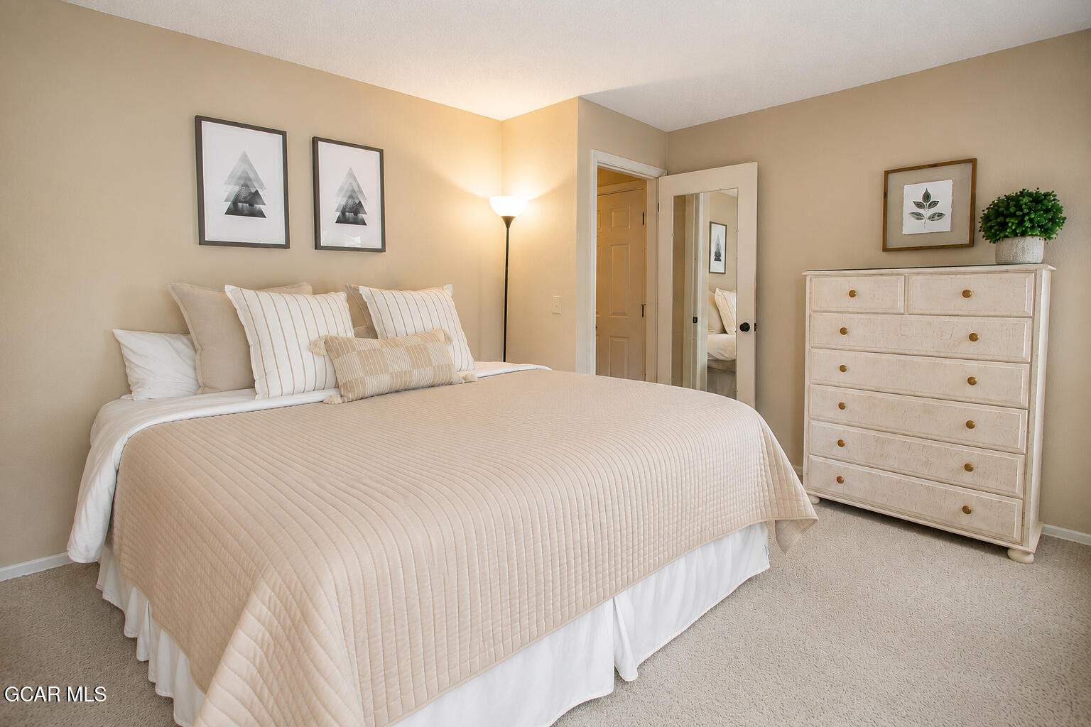 Bedroom with a neatly made bed, framed artwork, and white dresser.