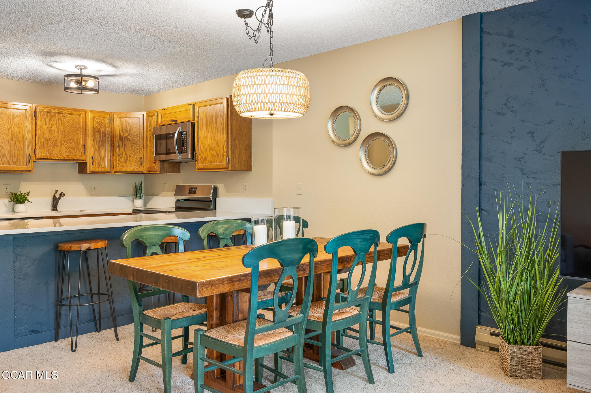 Dining area with a wooden table, teal chairs, and an adjoining kitchen with oak cabinets.