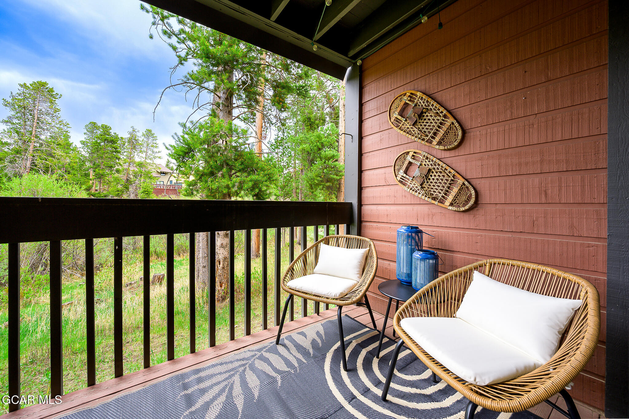 Covered balcony with wicker chairs, decorative snowshoes, and a wooded view.