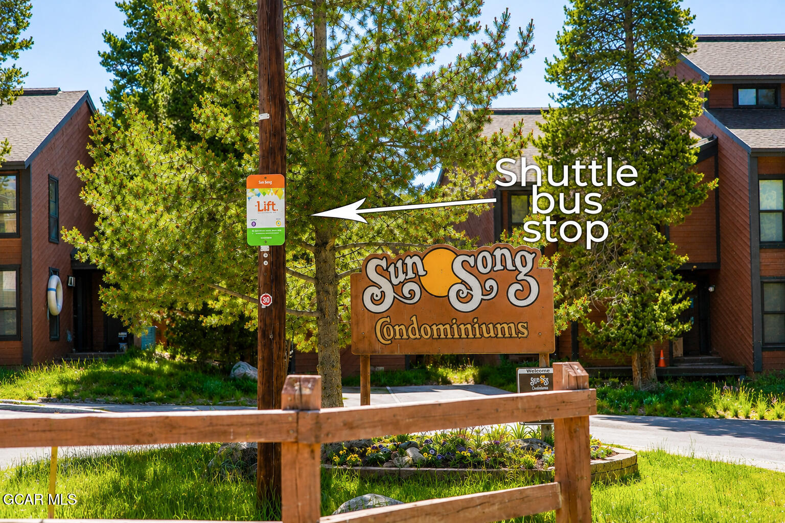 Sun Song condominiums beside a shuttle bus stop, framed by pine trees.