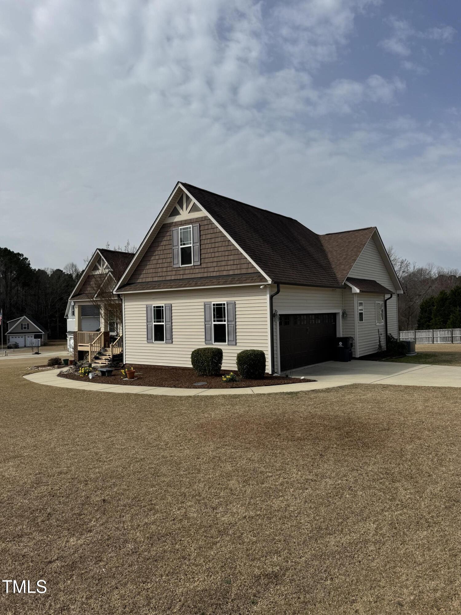 Beige two-story home with brown gables, dark attached garage, and curved walkway across a broad lawn.