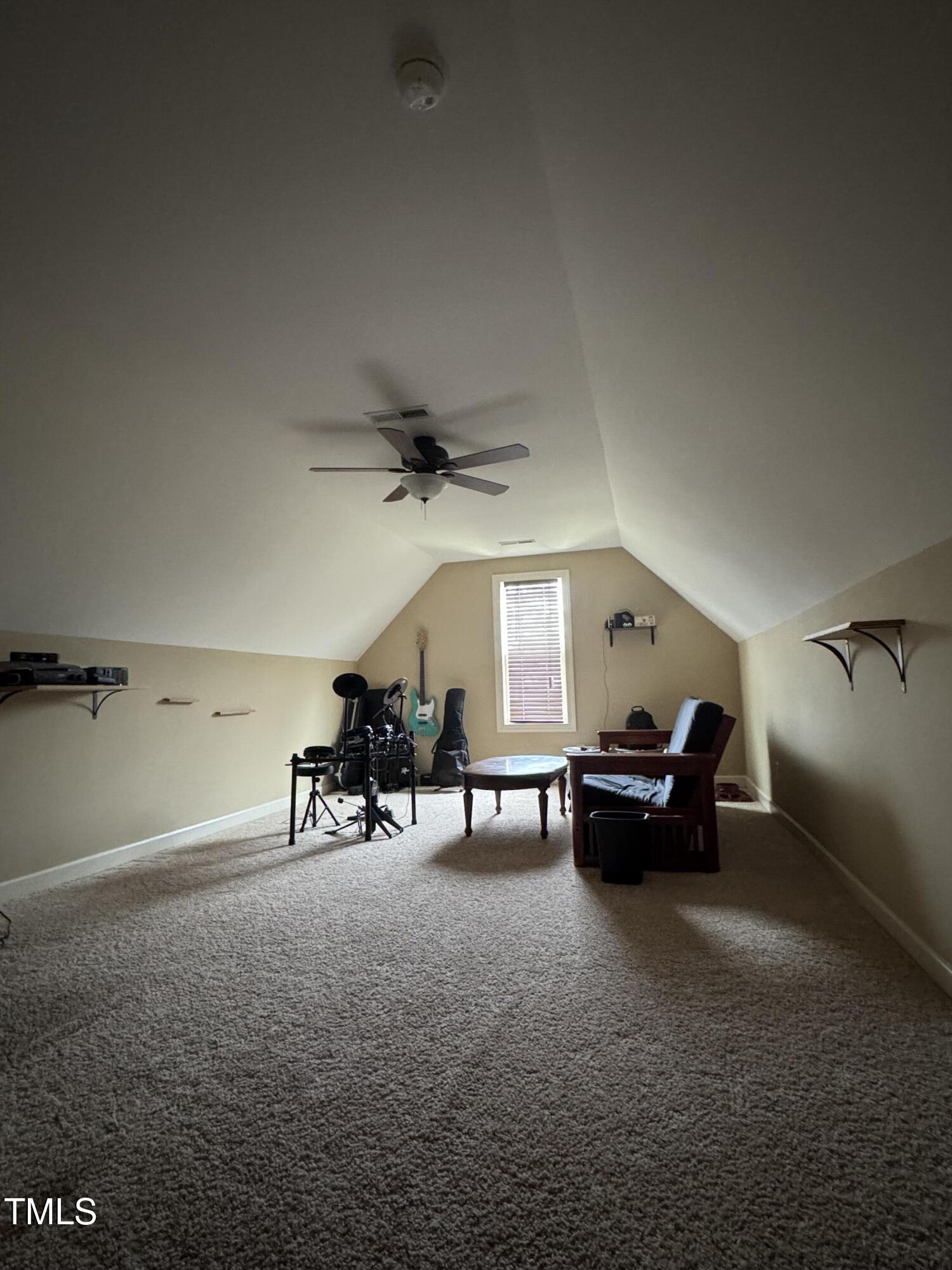 Carpeted bonus room with vaulted ceiling, drum kit, guitars, and seating area.