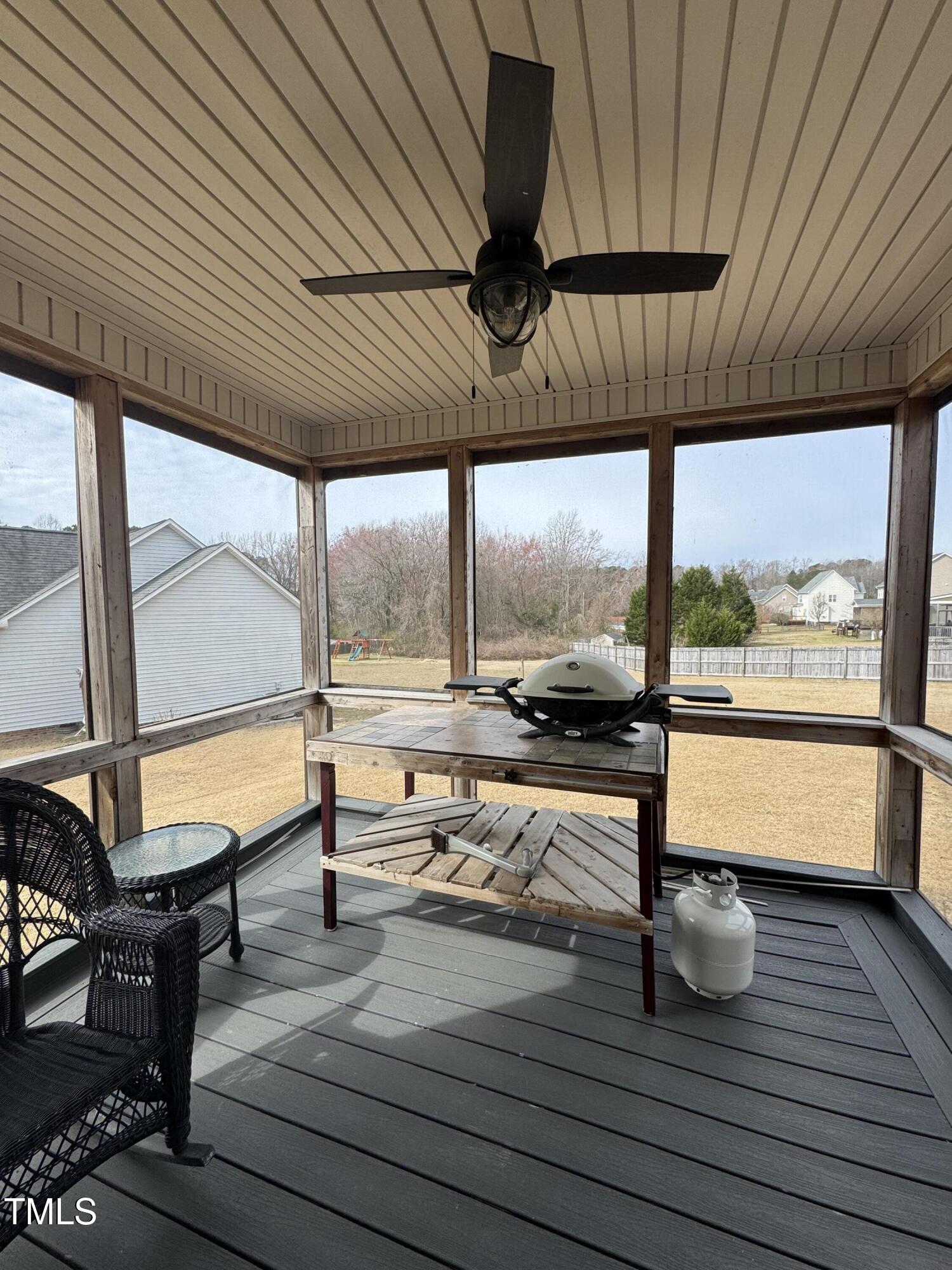 Screened porch with a ceiling fan, wicker chairs, and a grill overlooking the backyard.