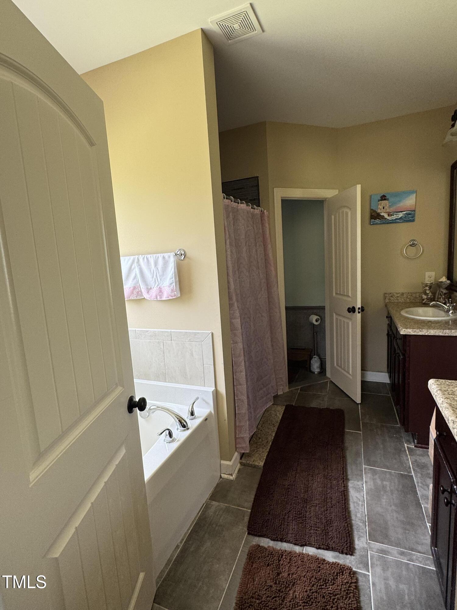 Bathroom with a tub, pink shower curtain, tiled floor, and granite vanity.