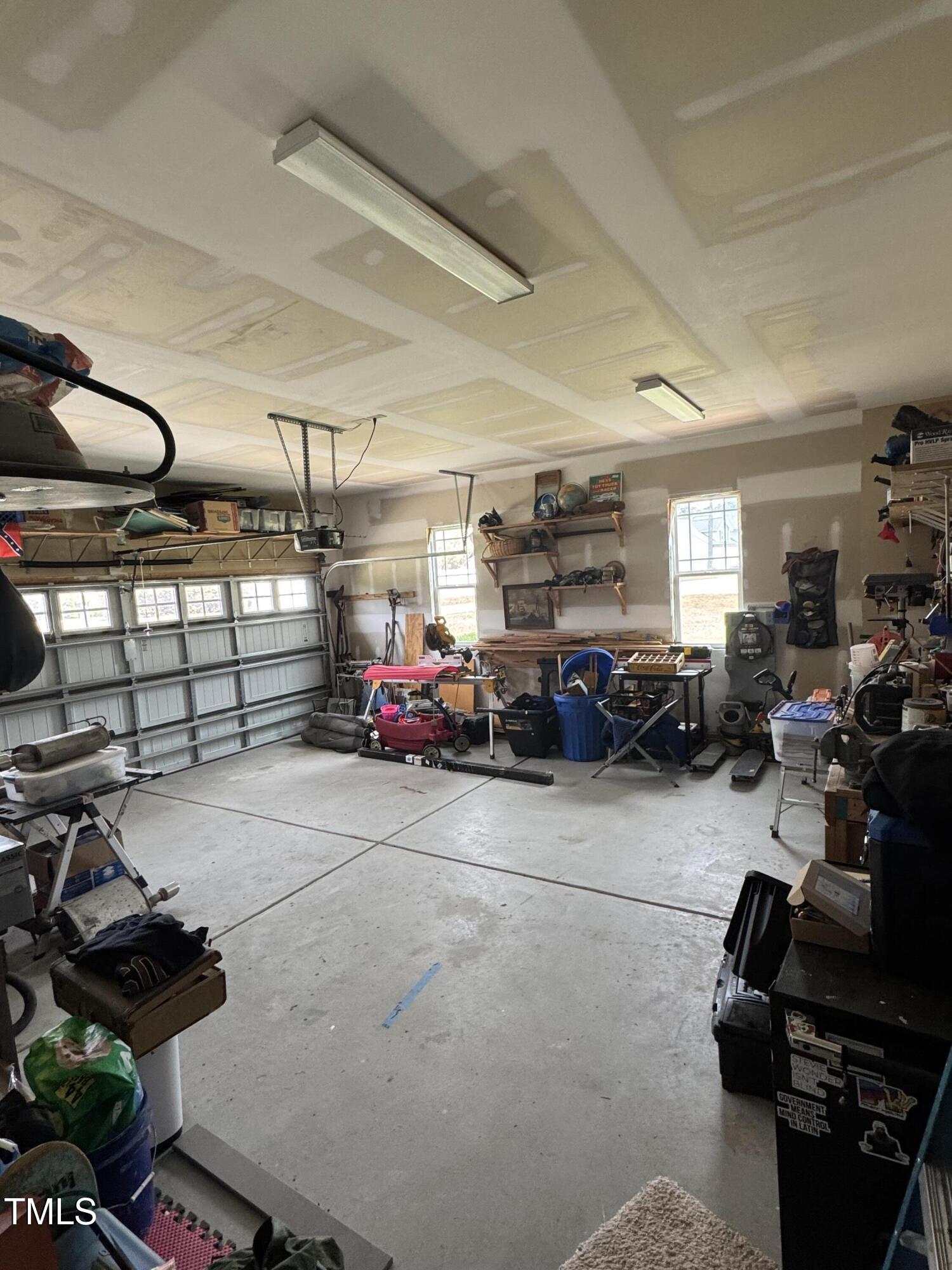 Spacious garage with a large garage door, concrete floor, and shelves crowded with tools and stored items.