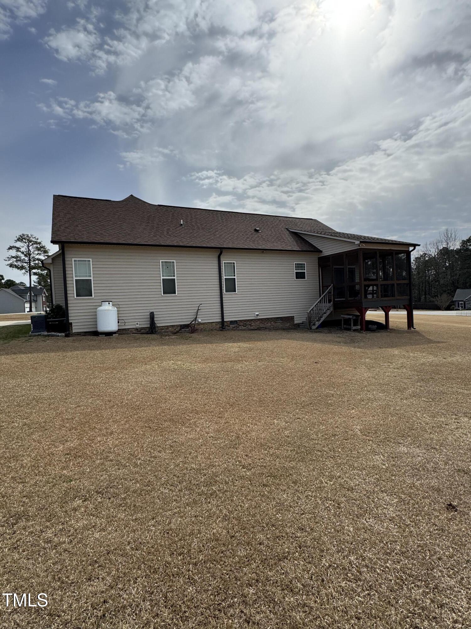 House exterior with a raised screened porch, stairs, and a broad dormant lawn.