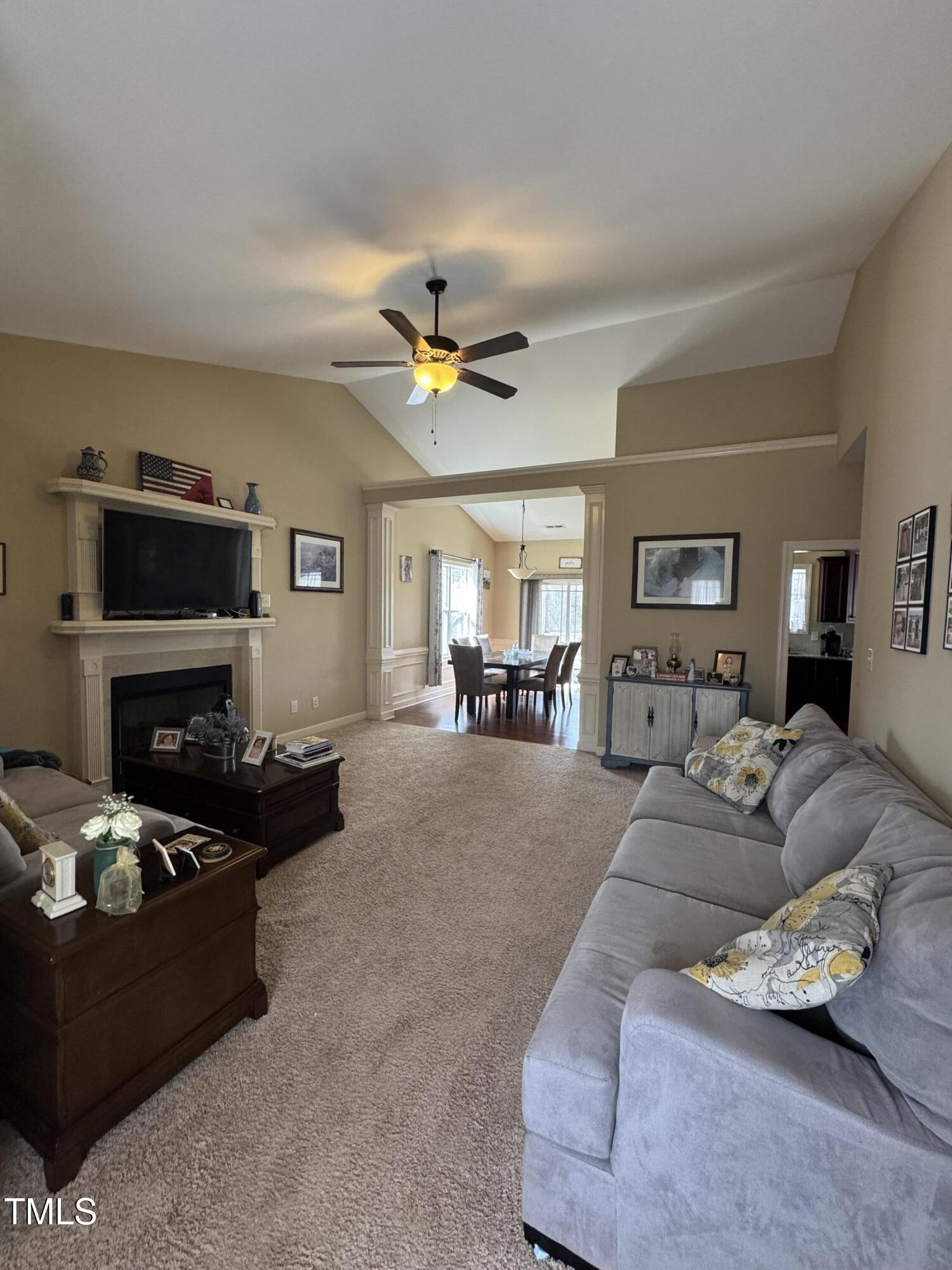 Living room with a vaulted ceiling, fireplace, television, and gray sectional opening to a dining area.