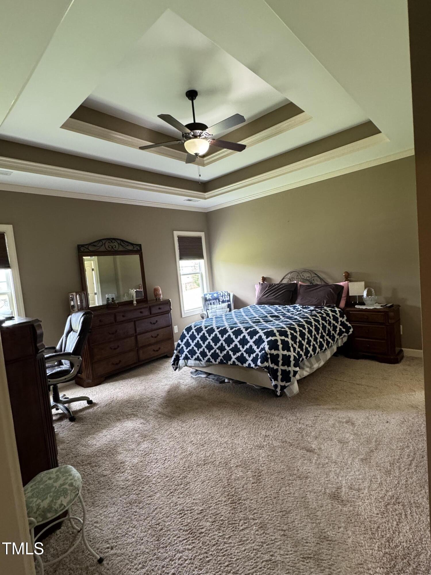 Bedroom with a patterned bedspread, dark wood furniture, and a tray ceiling with a ceiling fan.