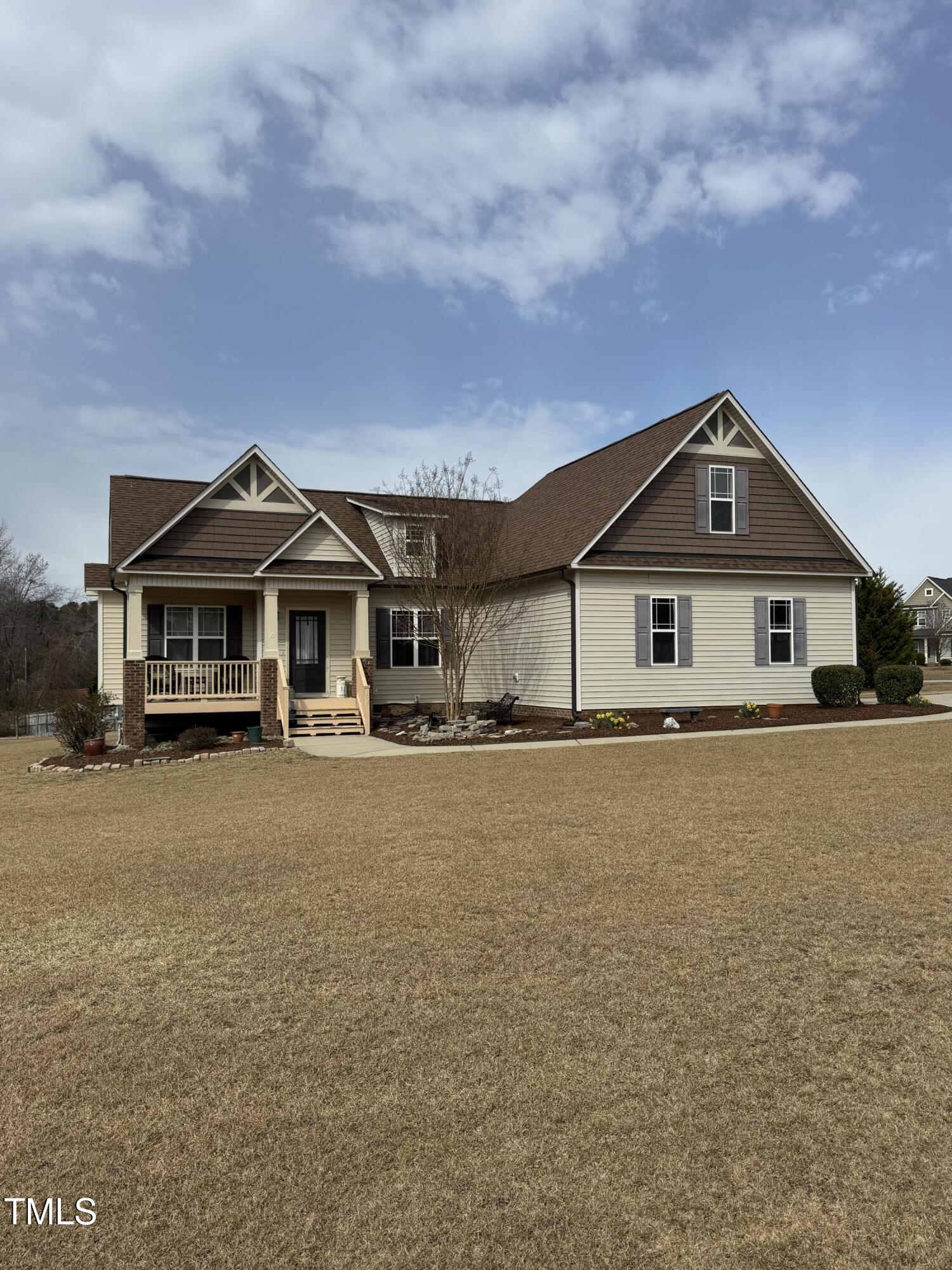 House with a brown gabled roof, covered front porch, and broad dormant lawn.