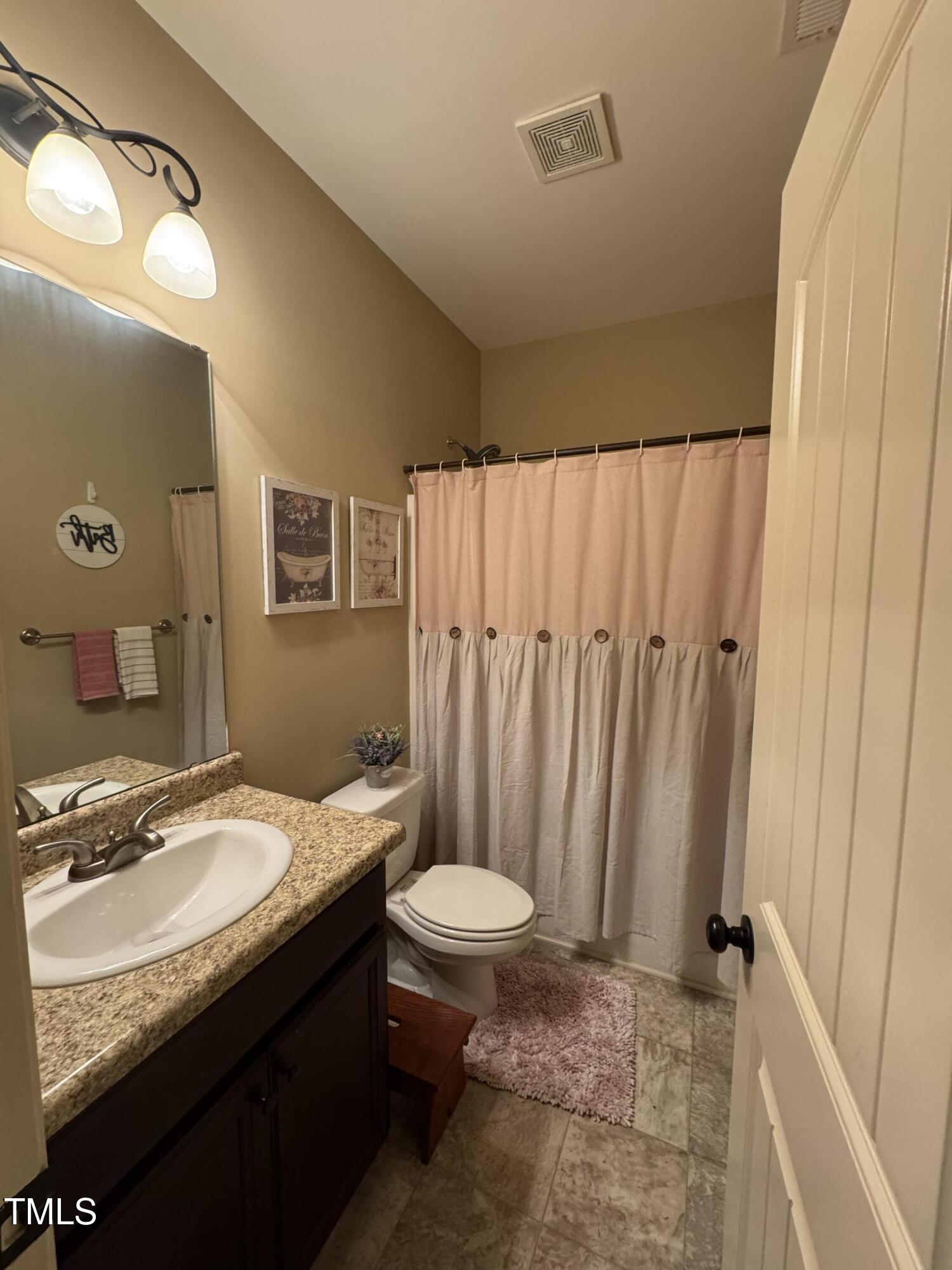 Bathroom with granite vanity, dark cabinets, and a pink-and-white shower curtain.