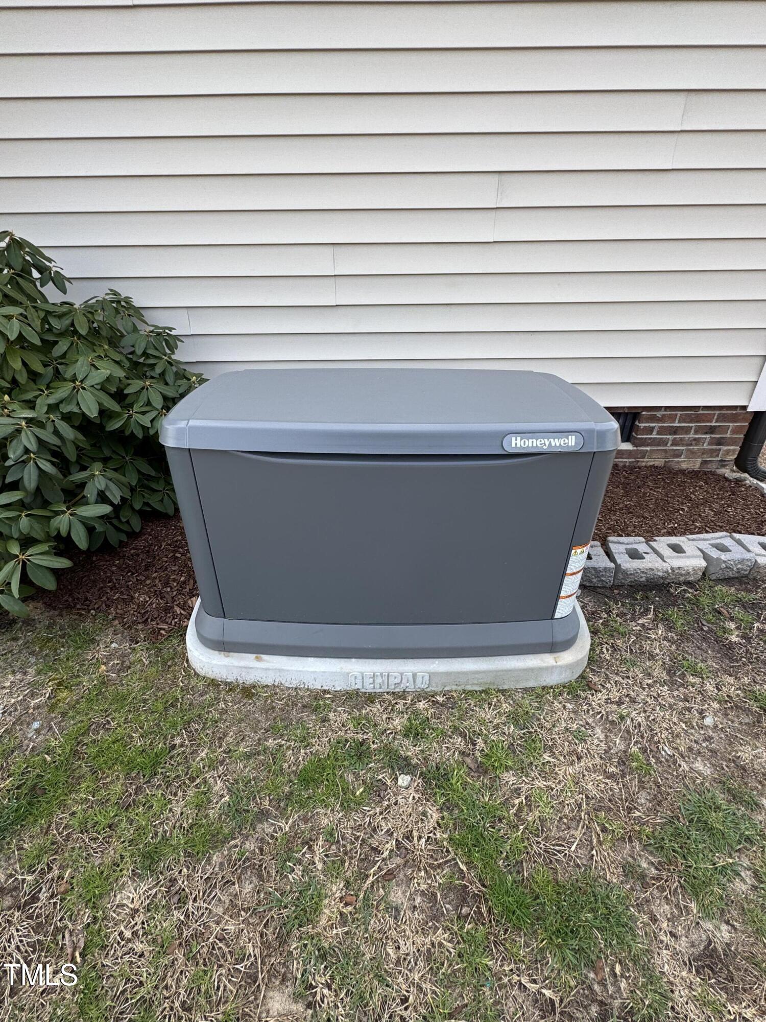 Gray Honeywell standby generator beside the home, mounted on a Generac concrete pad.