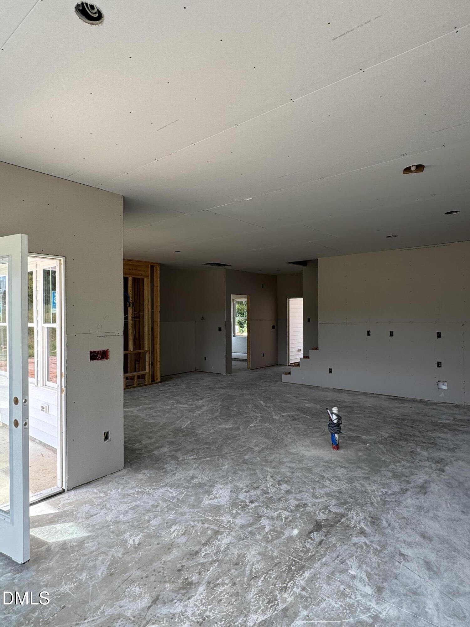 Unfinished open living area with exposed framing, drywall, and a concrete floor.