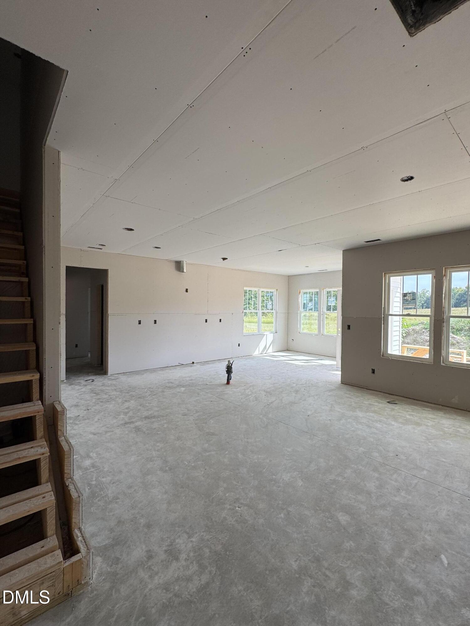 Unfinished open room with concrete flooring, exposed staircase, and large windows.