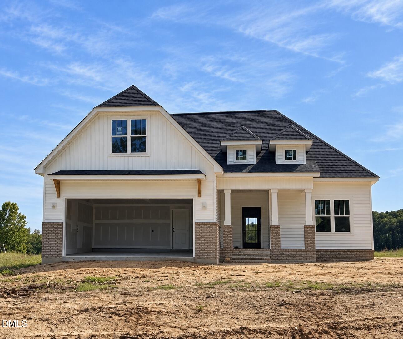 White house with brick accents, two roof dormers, and an open garage on a bare dirt lot.
