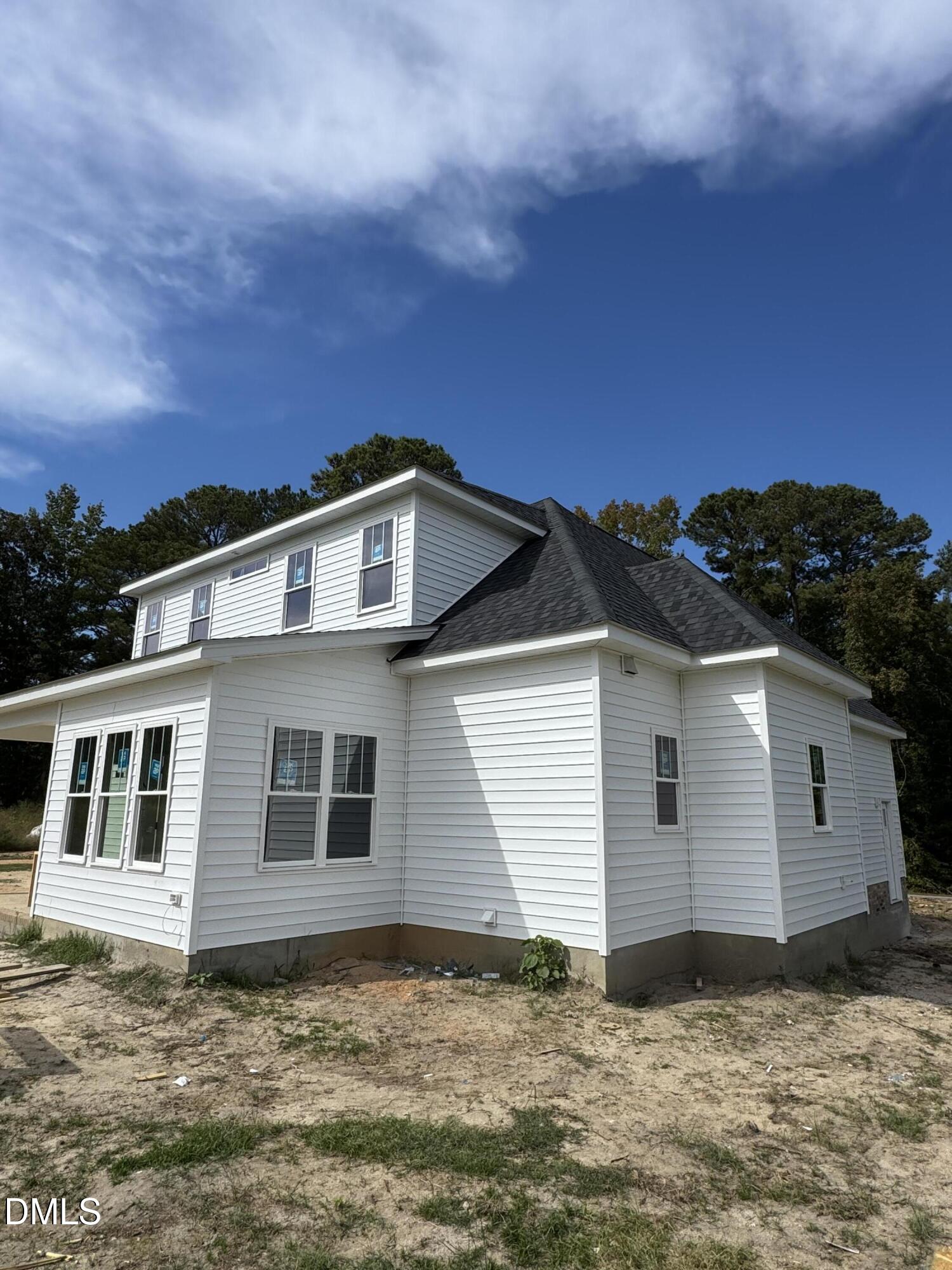 White two-story house with dark shingle roof, surrounded by bare soil and trees.