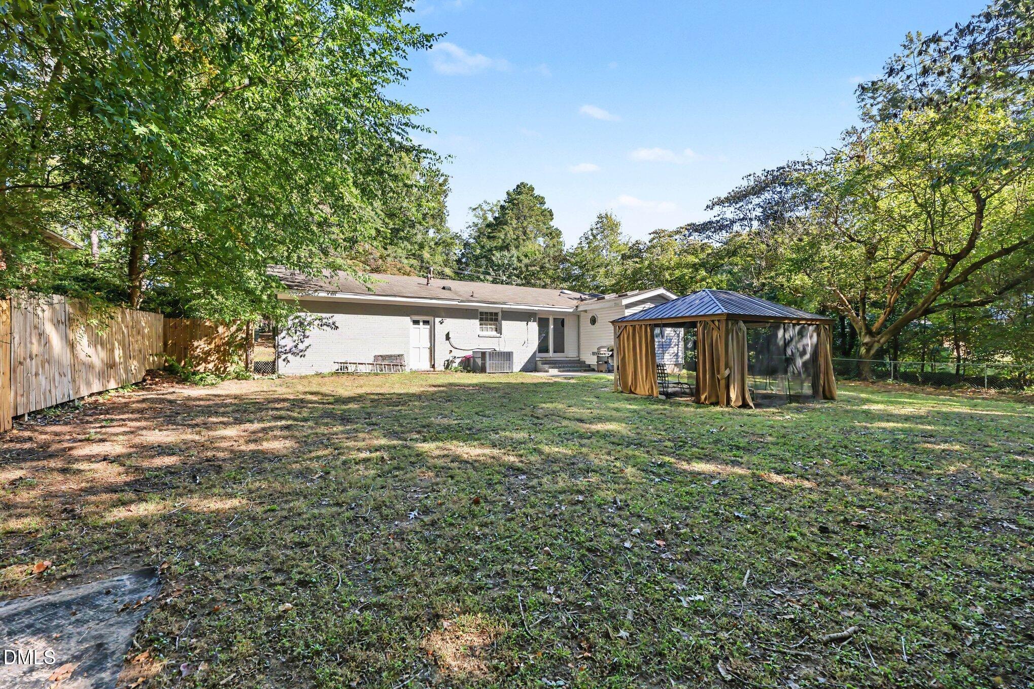 Rear of a single-story home with a tree-shaded lawn and curtained gazebo.